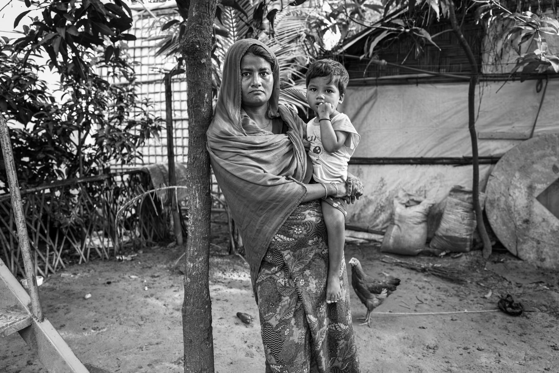 A Rohingya woman from Maungdaw stands with her child after recently fleeing Myanmar. She reports suffering from mental distress following the journey and the imprisonment of her husband in Sittwe. Kutupalong refugee camp, Cox's Bazar, Bangladesh, September 2025