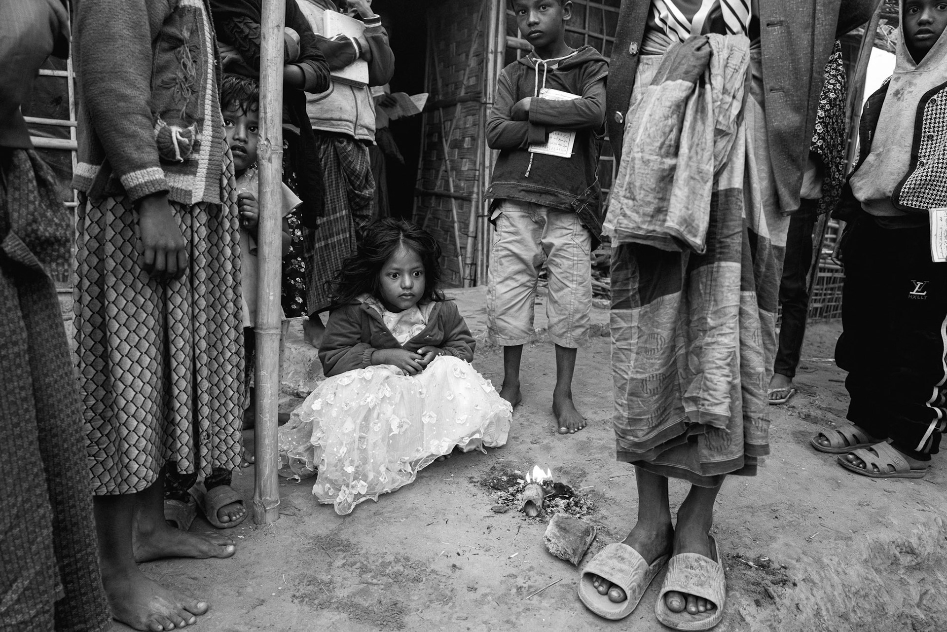 A group of children standing near a child seated on the ground in a communal area of Balukhali refugee camp in southern Bangladesh, January 2026