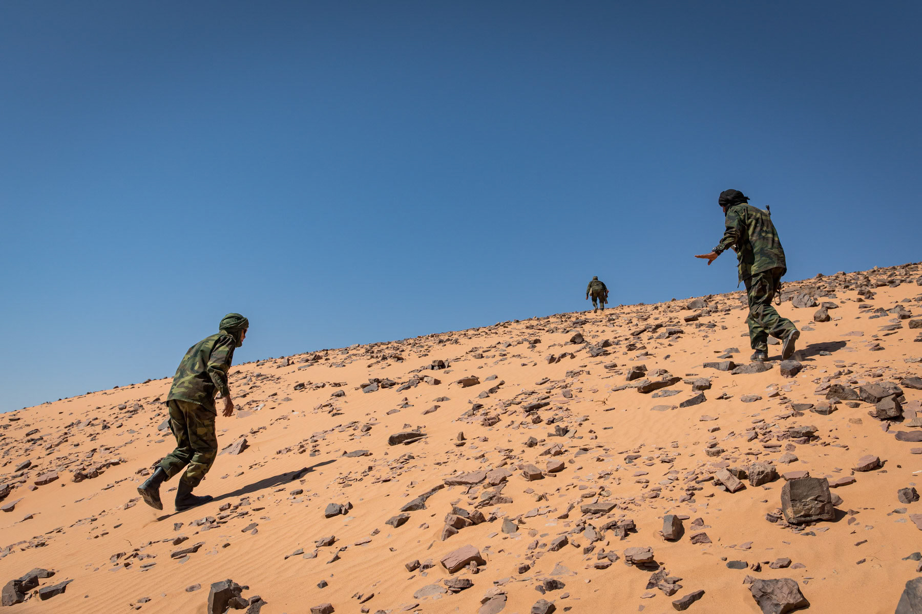 Sahrawi soldiers moving up a berm on the frontline to monitor the rocket impact they are about to launch towards Maroccan positions merely 5 km away and the 2,700 km long sand wall protection, built by Morocco, dividing the Western Sahara between the Moroccan controlled territories and Sahrawi liberated territories. Undisclosed location behind the frontline in the liberated Sahrawi territories, Sahrawi Arab Democratic Republic, October 2021