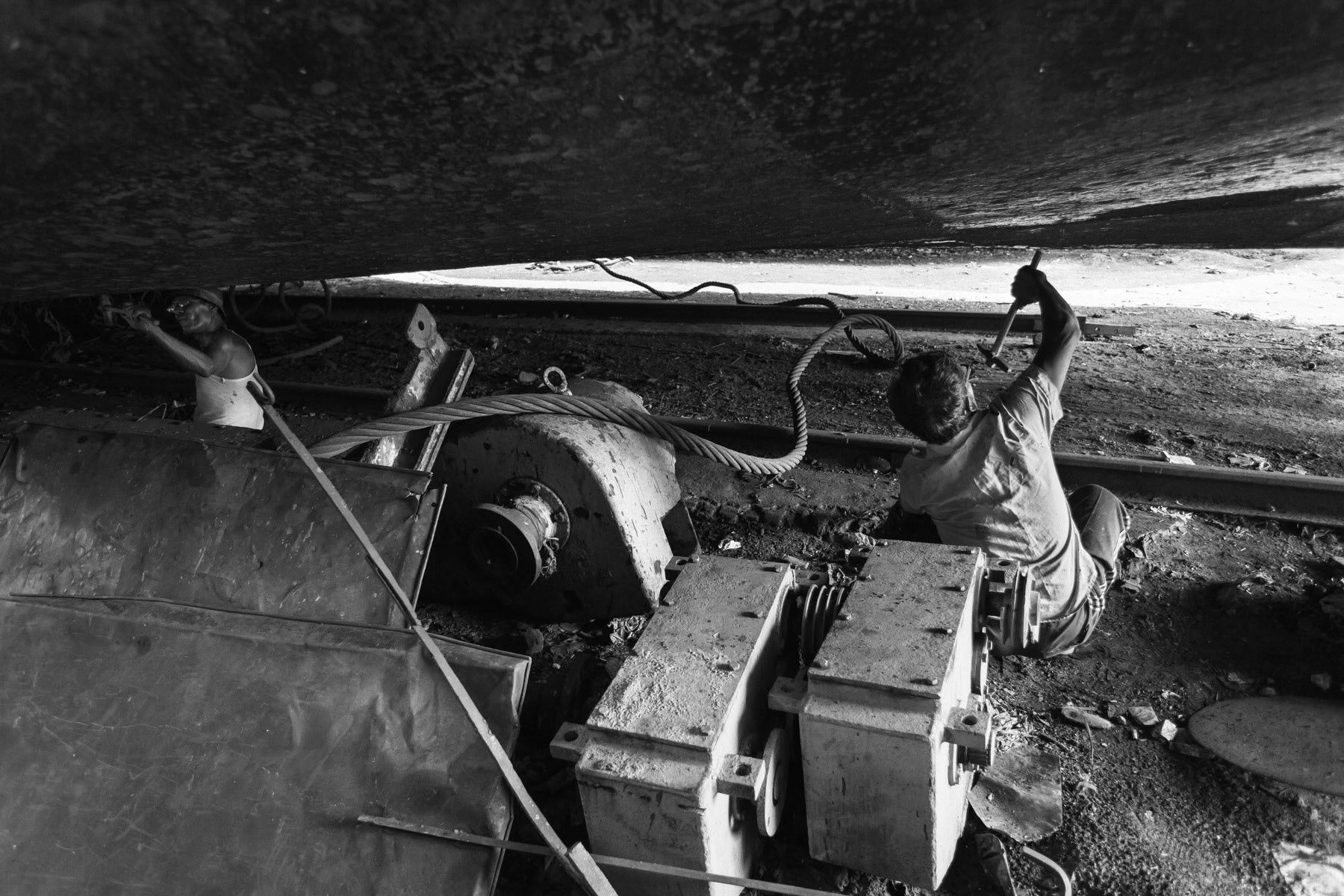 Shipyard workers removing manually old paint from the hull of a ferry boat, Dhaka shipyards, Bangladesh, October 2014