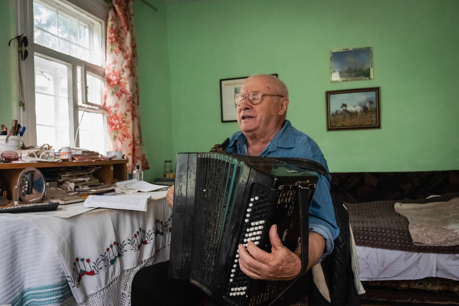Michaily playing and signing a song he composed as an ode to the liquidators and firefighters who gave their life to stop the radiation from reactor number 4 in 1986. Michaily Pavlovich is 84 years old, was an elementary school teacher. Worked in the late sixties and seventies several rural schools in the Chernobyl area. After the disaster in 1986 he teached in a school 200 km from Chernobyl until his retirement in 2000. He returned to his original house near Chernobyl but in order to be allowed back he had to have an occupation, so he dedicated his time as a musician and singer for the church in Chernobyl. To this date he writes songs and continues to entertain people. Self settler, Chernobyl, Ukraine, September 2021