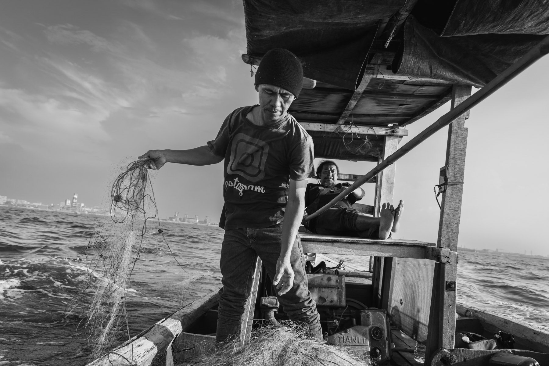 Fisherman from Muara Angke at work, placing his 1 km long fishing net in the Jakarta Bay. Mass construction along the shore of the Jakarta Bay and the creation of artificial islands has depleted the fish stocks, changed the currents, and blocked the outflow of rivers provoking regular floods in the Northern neighbourhoods of Jakarta. Bay of Jakarta, Indonesia, June 2022