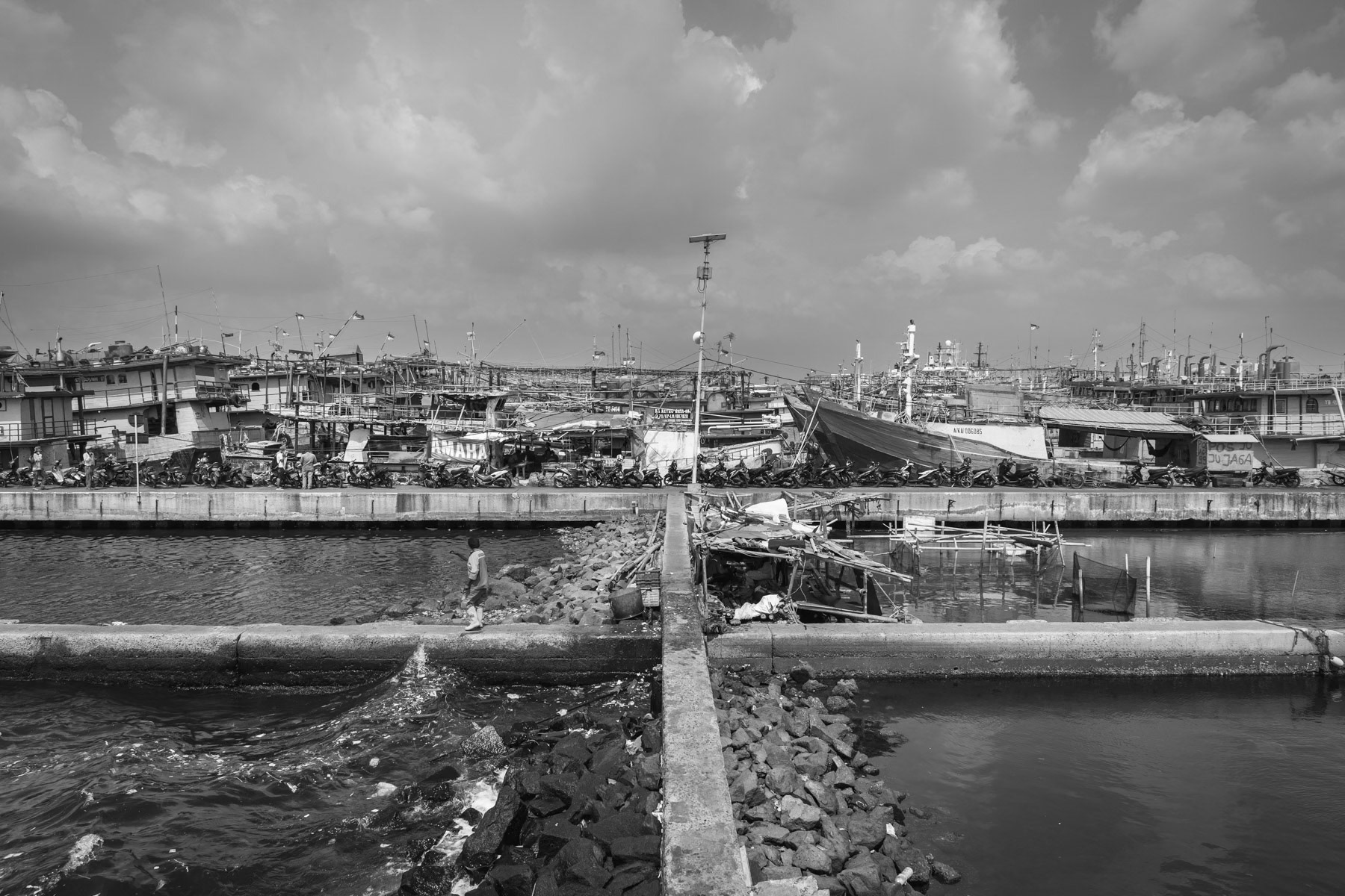 Fishing port of Muara Buru, a neighbourhood along the seashore that is partly protected by a seawall against rising sea levels and sinking soil. The soil is sinking at a rate of 10 to 20cm per year. The unstability of the ground is provoked by widespread drilling of water wells for new real estate projects, creating huge air pockets once the water is exhausted. Most of the lands in North Jakarta lay up to 2 metres under sea level. Jakarta, Indonesia, June 2022