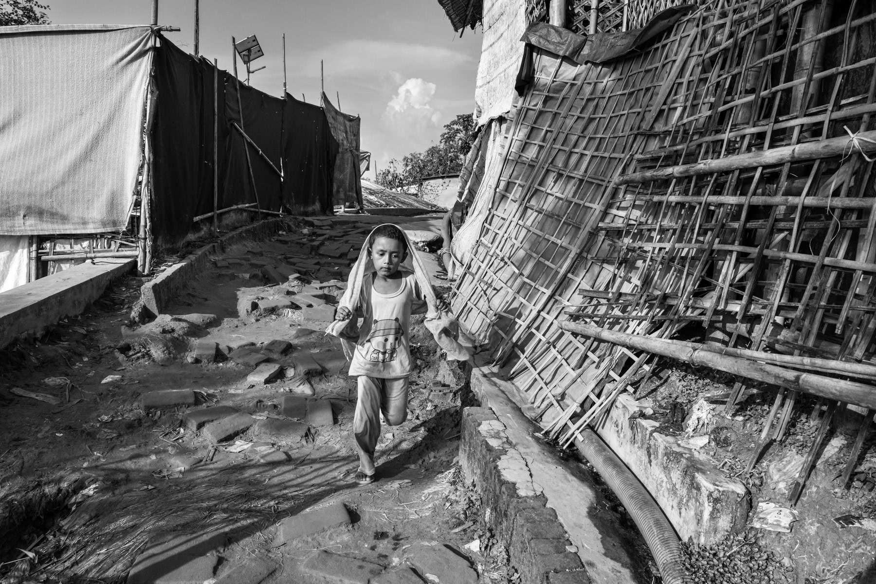 A Rohingya girl runs downhill along a paved alley in the camp, part of a settlement now hosting well over **1 million refugees**, making it the largest refugee camp in the world. Since 2024, at least **150,000 more Rohingya** have fled violence carried out by the Arakan Army (AA). Kutupalong refugee camp, Ukhiya, Bangladesh, September 2025