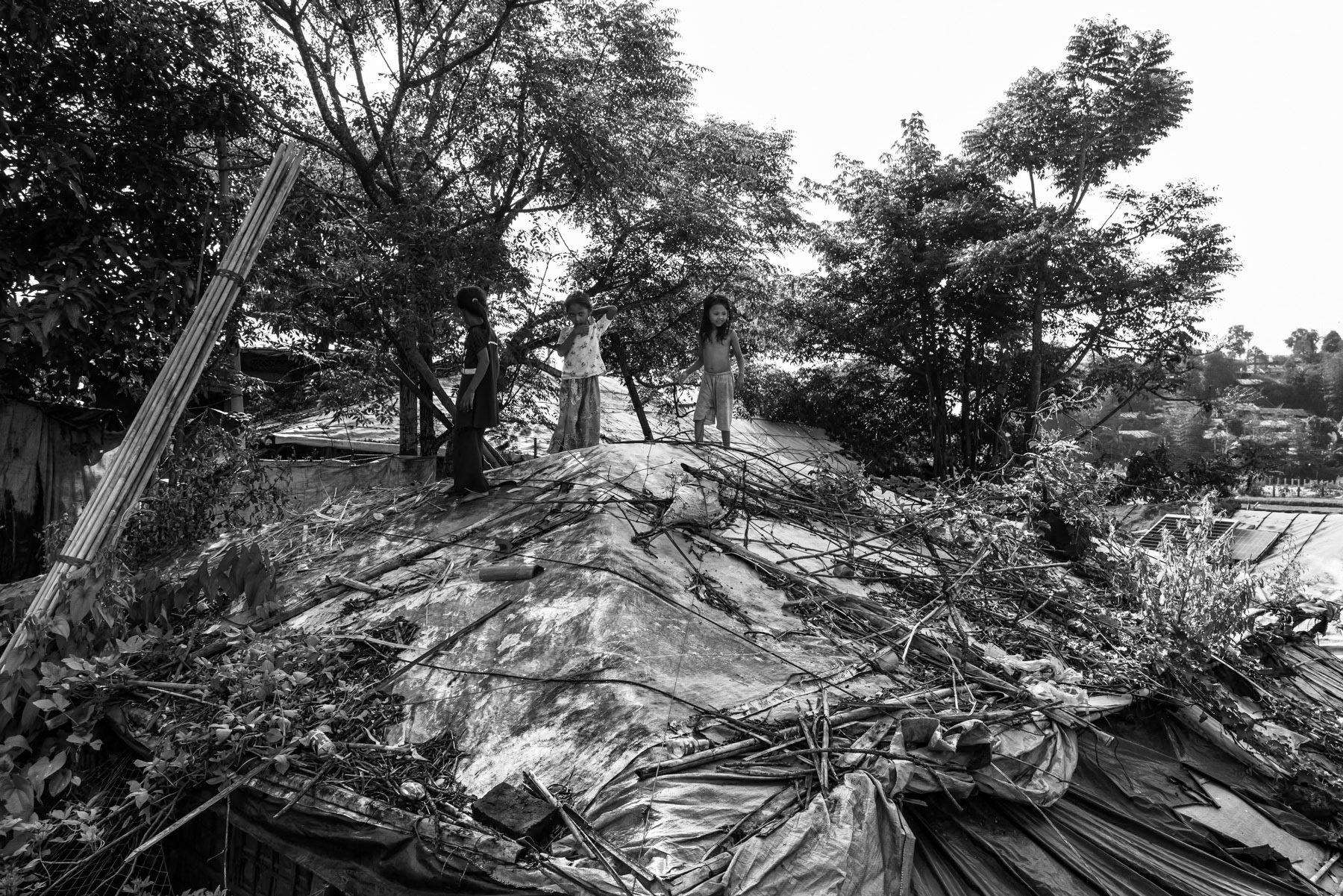 Three Rohingya girls play on the roof of a plastic-sheeting shelter in the refugee camp. Kutupalong refugee camp, Cox's Bazar, Bangladesh, September 2025