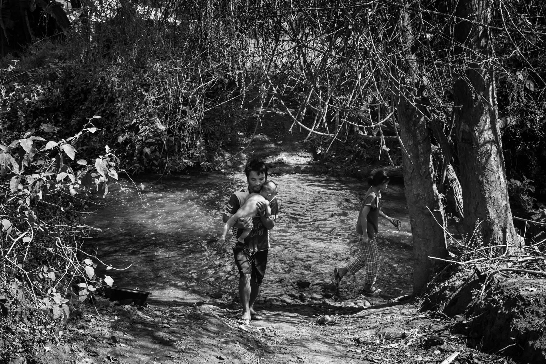 Parents cooling their child in the river to bring down a high fever. Kanele Htaw IDP camp, Kayin State, Myanmar, January 2024