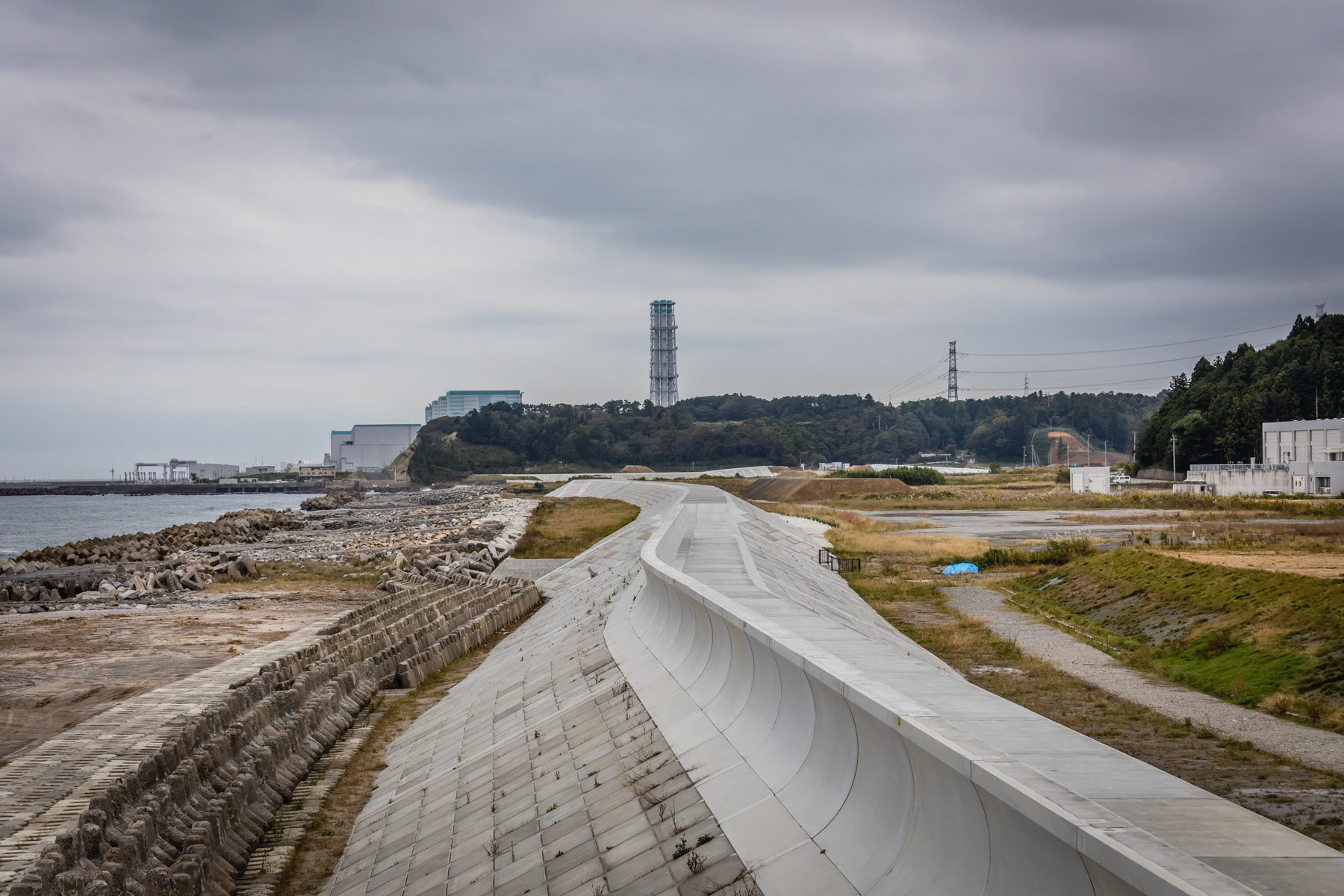Tomioka port and its protective sea wall with Fukushima Daini Power Plant in the background. Contrary to the Daichi plant, Daini has been shut down in a controlled way and is in the long term phase of being decomissioned. Tomioka, Fukushima Prefecture, Japan, October 2019