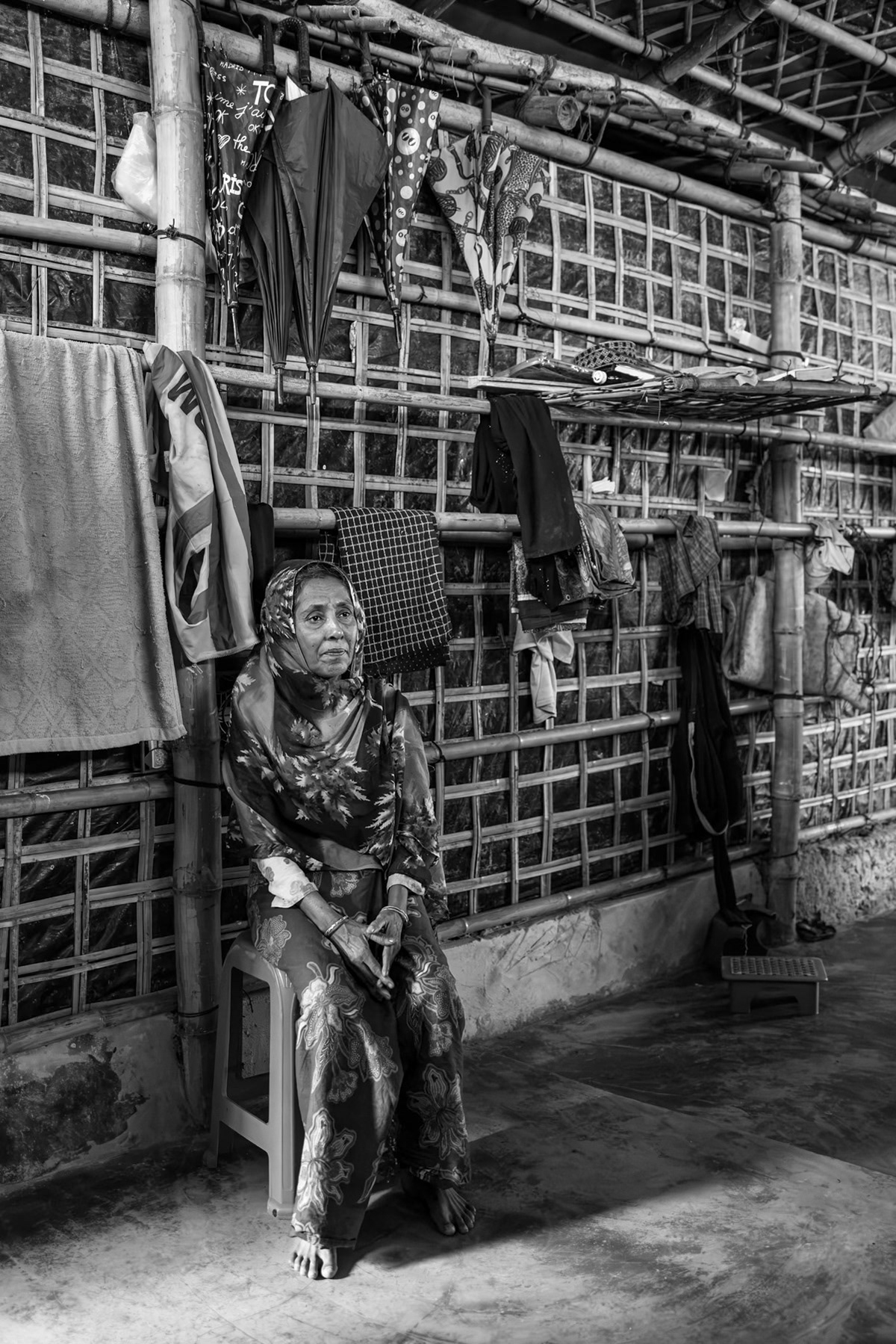 Alomara, 60, from Laway Daung in Buthidaung Township, sits in her shelter in the refugee camp after fleeing Myanmar. She and her family left their village on 14 May 2024 and sheltered in Ward 5 of Buthidaung for seven months before continuing their escape. They arrived in Bangladesh on 17 December 2024. Though none of the nine family members traveling with her were injured, she reports that a brother and sister were killed during the attack on their village, and that the family had no access to food while fleeing toward the border. Kutupalong refugee camp, Ukhiya, Bangladesh, September 2025