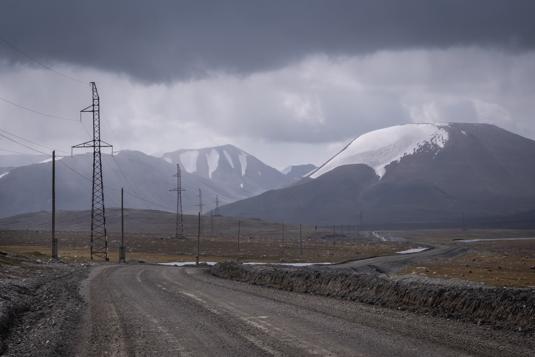 High altitude road with melting glaciers on the background. Climate warming paired with longer periods of drought have in the past decennia accelerated the disappearance of Kyrgyz and Tajik glaciers provoking land slides, floods and destruction of entire communities. Road to the Kumtor gold mine, 4000m altitude, Barskoon valley, Kyrgyzstan, August 2021