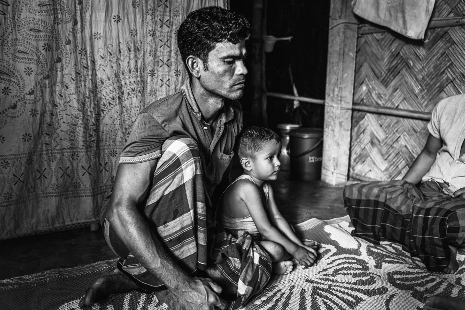 Anamullah, 40, from Shida Fara in Maungdaw Township, with his youngest son after being injured in the leg by a drone strike while fleeing Myanmar. His wife and other children fled with him, arriving in Bangladesh on 20 August 2024. Before displacement, Anamullah worked as a warehouse daily worker for the ICRC. Kutupalong refugee camp, Ukhiya, Bangladesh, September 2025