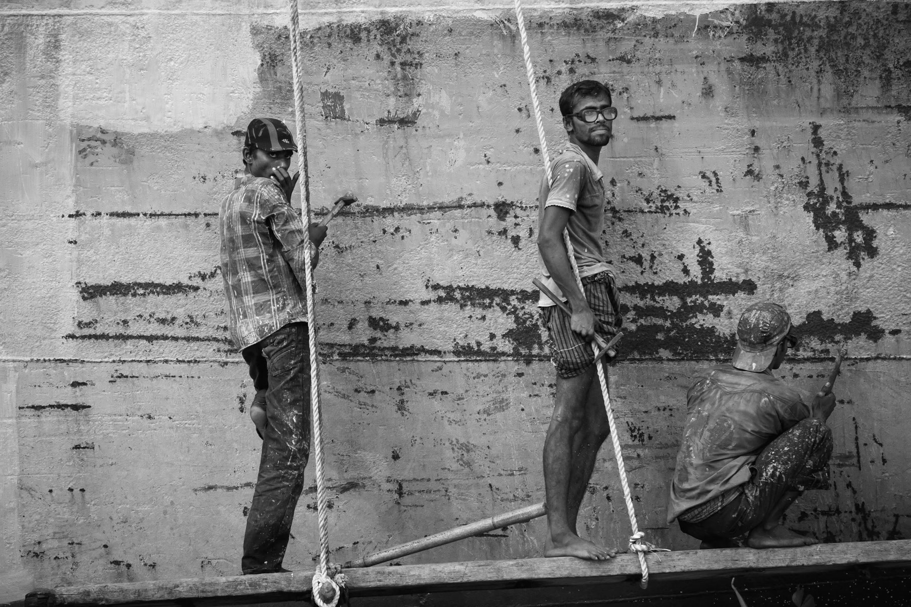Shipyard workers removing paint with a hammer from a cargo ship on the Buriganga river, Dhaka, Bangladesh, October 2014
