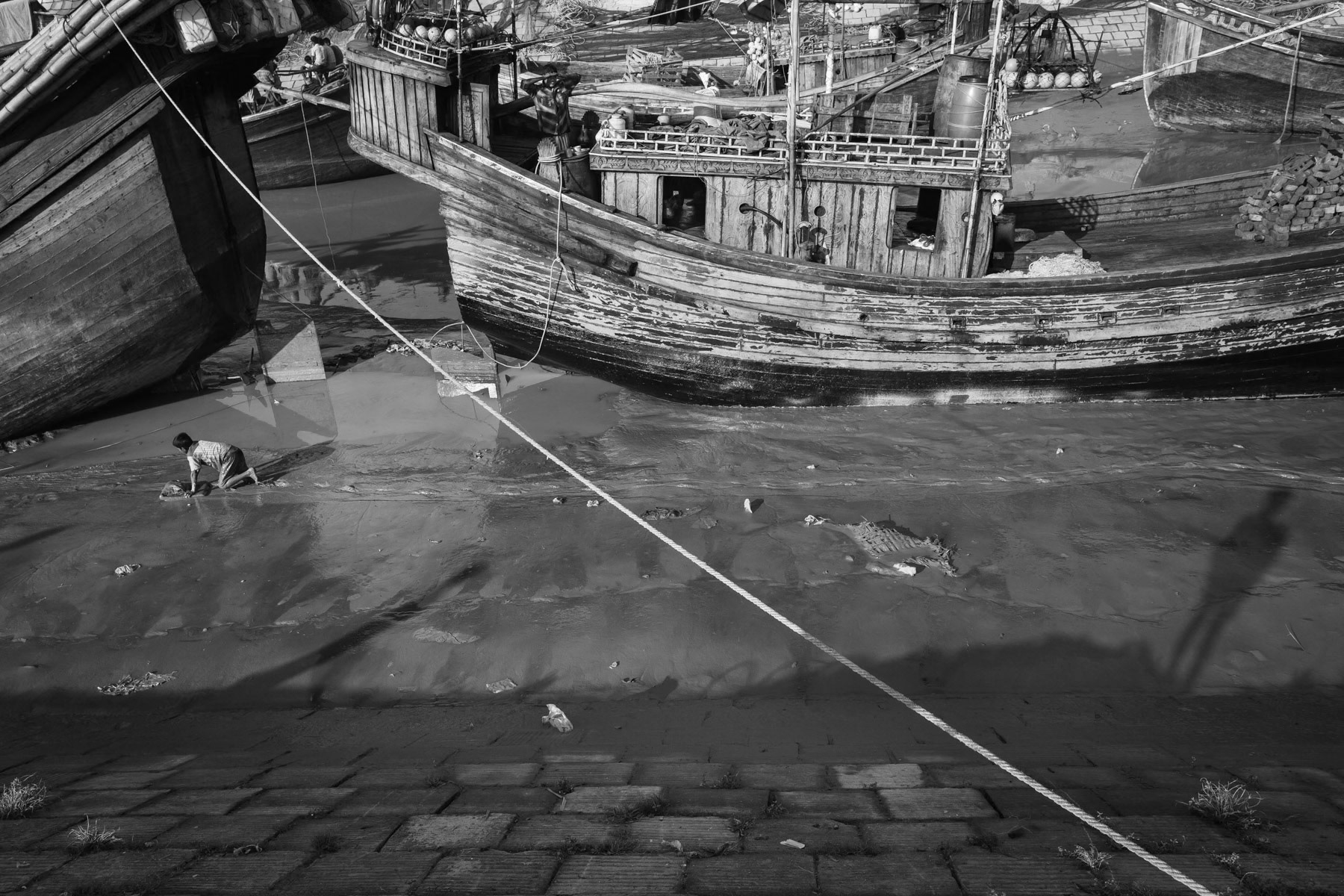 Boy looking for small fish in river silt, fishing port along the Karnaphuli river, Chittagong, October 2014