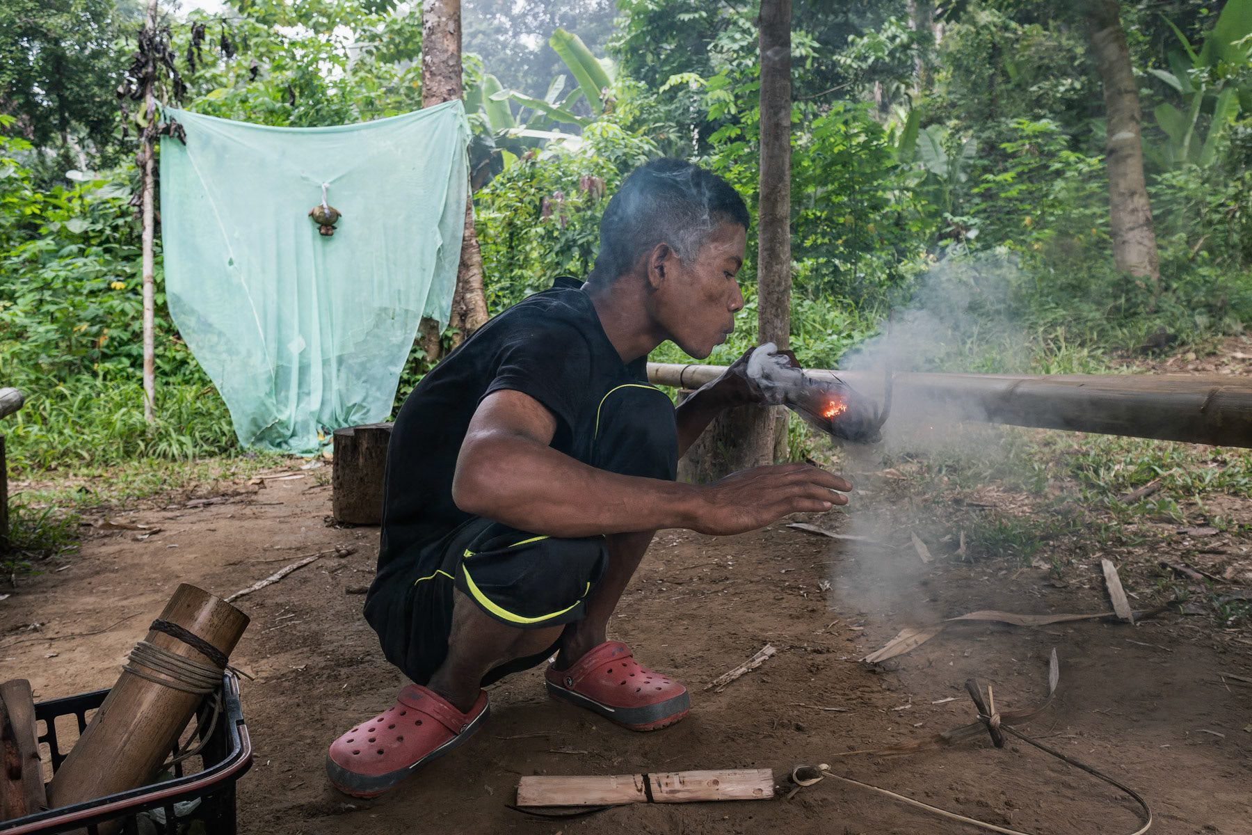 A young adult of the indigenous Bateq community making fire with rattan and mahagonia wood. Orang Asli village in the Taman Negara rainforest. Pahang, Malaysia, June 2023