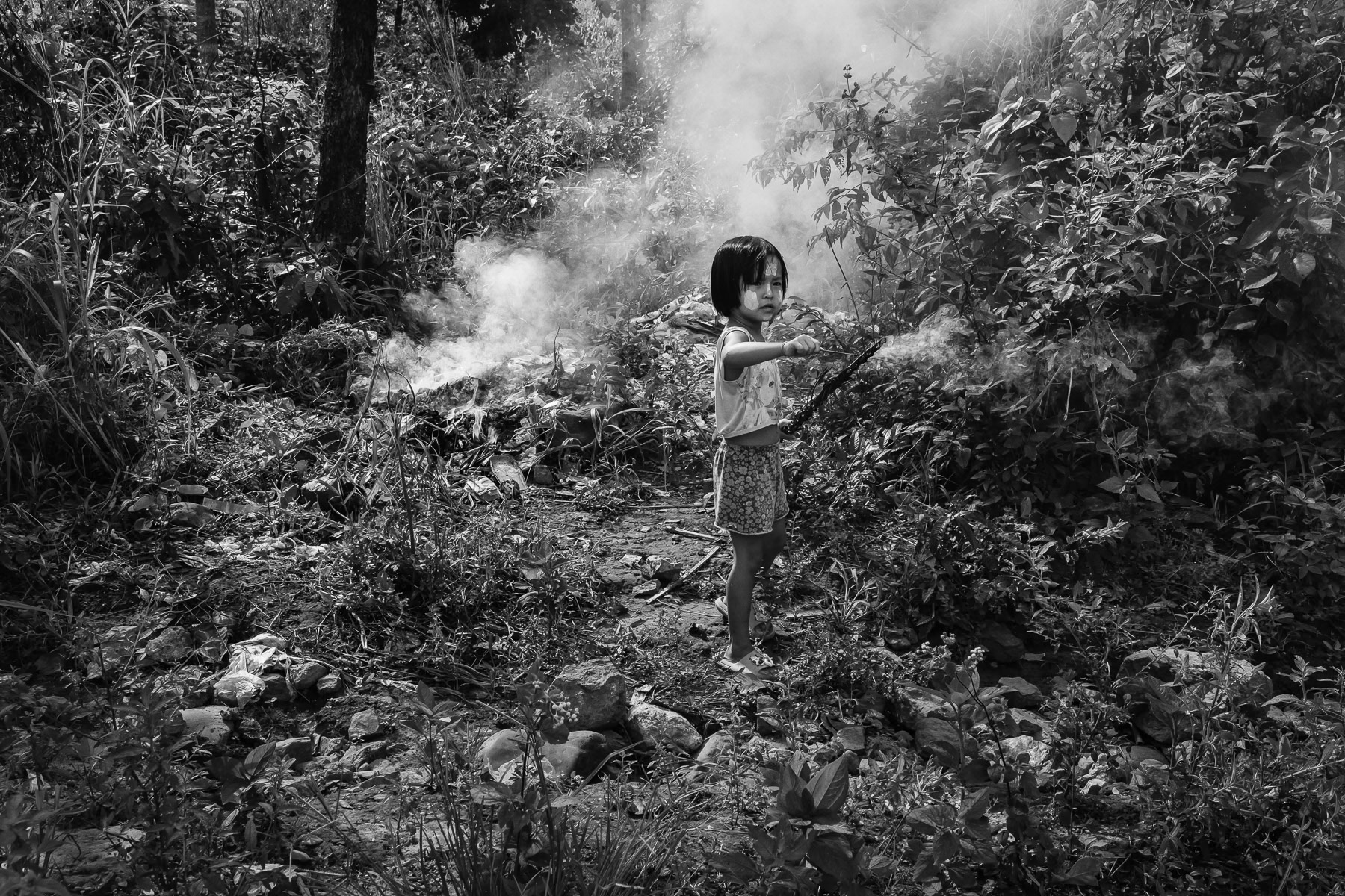 A young girl from the Karen ethnic minority burning waste at a IDP camp for people displaced by the conflict in Myanmar. Htee Baw Kaw IDP camp for displaced people from nearby Wale town. Karen State, Burma, September 2024