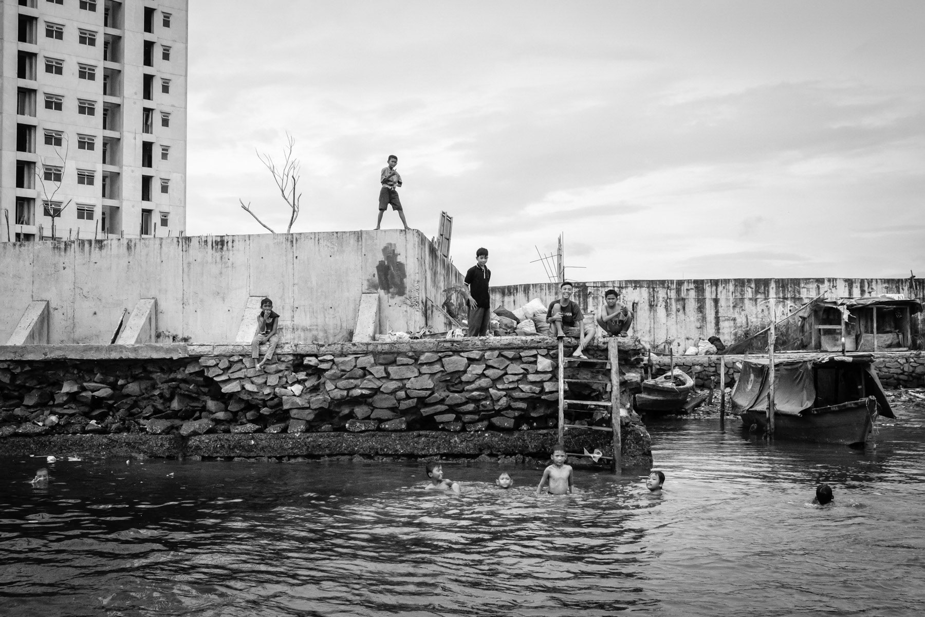 Kids playing and swimming along the seawall built to keep seawater out of the city. As most of North Jakarta lays under the sea level, sea water needs to be kept out and river outflow needs to be pumped out as a prevention for floods. Jakarta, Indonesia, March 2020