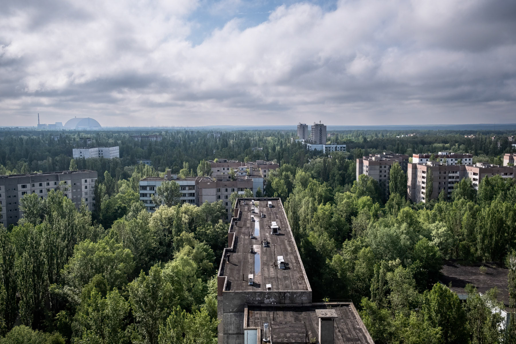Pripyat residential buildings with reactor number 4 and its protection dome in the background. Pripyat was build as a satelite town only 6 km from the NPP. The complete population of Pipyat was evacuated 36 hours after the disaster to never return again. Pripyat is now an overgrown ghost town where time stood still on 27 April 1986. Pripyat, Chernobyl NPP, Ukraine, June 2021