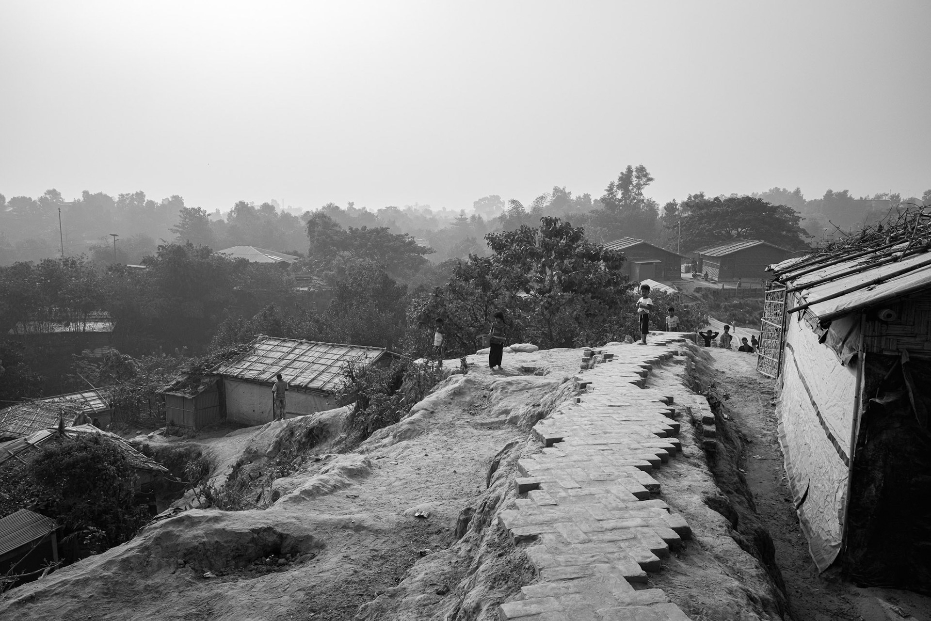 An elevated view of the brick-paved "interceptor" paths. These paths are vital arteries for a population that has been stripped of its freedom of movement and remains entirely dependent on humanitarian corridors. Kutupalong camp, Bangladesh, January 2026