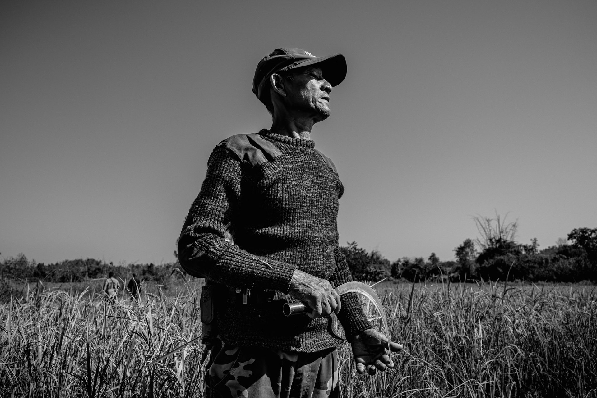 A KNLA member stands at the edge of a rice field near the Wale frontline. Even during agricultural cycles, the landscape is a potential battleground, monitored by a military that increasingly uses drones to strike beyond the forest's edge. Kayin State, Myanmar, January 2026