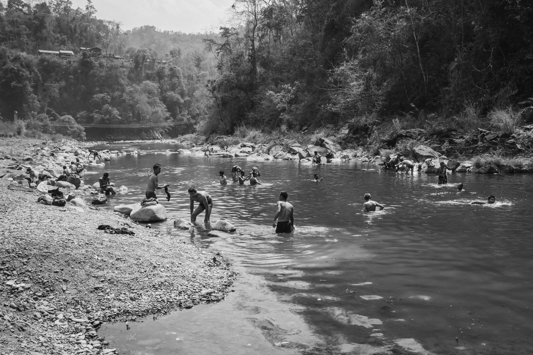 Prisoners of war (POW) bathing and washing their clothes in the river. Contrary to the Myanmar military that executes prisoners the Chin National Army provides them shelter and food and follows the Geneva conventions related to POW. Camp Victoria, Chin State, Myanmar, April 2024