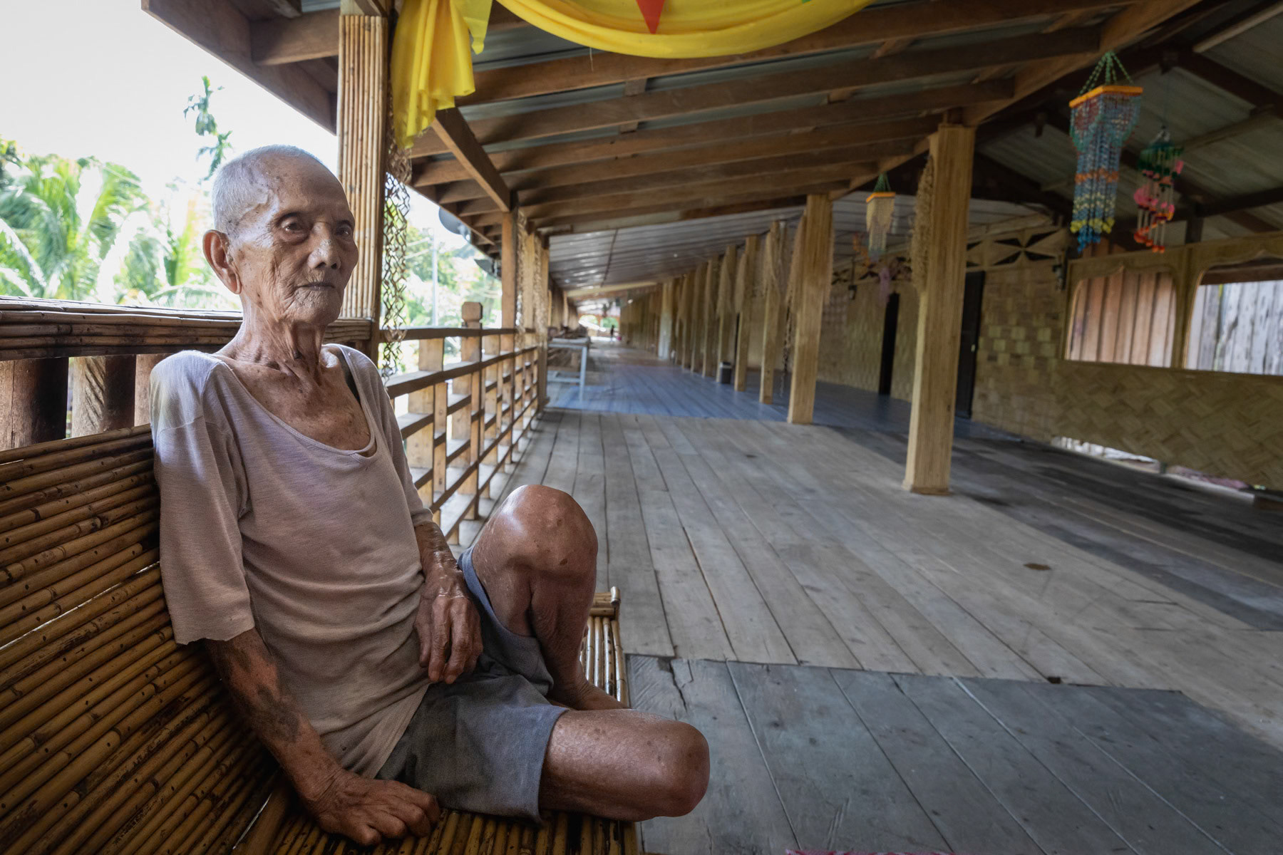 The elder, 100 years, of the Bukit tribe. The Bukit tribe was originally living in the tropical rainforest. During the past decennia mine exploitation, logging and hydroelectric infrastructure have severely jeopardized their way of life and livelihood. Through re-settlement projects they are mostly living in small community clusters at the edge of the rainforest. Origianlly Pagan, the indigenous communities have been converted to Christianism throughout the 20th century, but nevertheless keeping many Pagan traditions and signs. Bukat settlement, Sarawak, Malaysian Borneo, June 2022