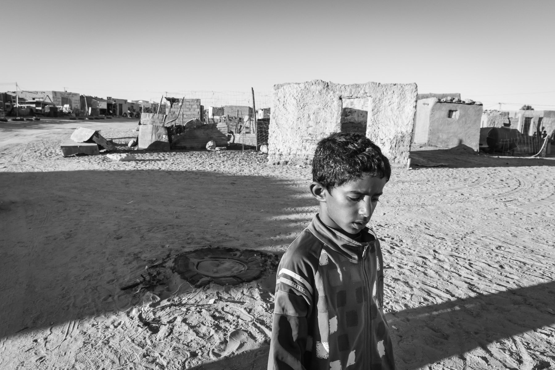 The Western Sahara protracted conflict between the Polisario Front and the Kingdom of Morocco started from an insurgency by the Polisario against the occupying Spanish colonial forces from 1973 to 1975 and the subsequent Western Sahara War against Morocco that lasted from 1975 to 1991. The armed conflict escalated in full war with the withdrawel of Spain from the area. The Polisario Front, backed by Algeria, waged a 16 year-long war for independence against the invading forces of Mauritania and Morocco. In 1976, the Polisario Front declared the establishment of the Saharawi Arab Democratic Republic (SADR), which was not admitted into the United Nations, but won recognition from a number of other states, mainly in Africa and Latin America. In 1979, Mauritania withdrew from the conflict and the territories it was occupying, leaving only Moroccan forces and the Polisario in the disputed territory. Finally after 16 years of war, a cease-fire agreement was reached in 1991.Since then until now most of the Western Sahara remained under Moroccan control, while the Polisario controls only 20% of the territory as the Saharawi Arab Democratic Republic with an additional area in Algeria where the Saharawi Refugee camps and the SADR government in exile is vested. At present most of the Western Sahara, the entire coastal area and its unlimited valuable mineral resources are controlled and settled by the Moroccan government and considered an intergral part of the Moroccan territory as the "Southern Provinces". This de facto territorial annexation has not been recognised by the United Nations or any other State. Morocco has, as early as 1979, been building a 2,700 Km long sand wall separating it from the Polisario controlled areas but also cutting all communication between Saharawi nomadic communities used to roam freely the desert. Also, an estimated 5 to 7 million landmines have been laid along the wall making it the longest active security wall in the world and one of the most heavily mined areas on the planet. It is often refered to as the wall of shame. The Saharawi refugee camps in Tindouf, Algeria, are a cluster of 5 refugee camps spread out in a very remote desertic area. The camps were established in 1975-76 for Saharawi refugees fleeing advancing Moroccan and Mauritanian troops. Most of the original refugees with an additional two generations are still living in the camps, making it one of the most protracted and forgotten refugee crisis in the world. An estimated 150,000 Saharawi refugees live today in the camps, where it is nearly impossible to sustain basic life. Food, water, building materials, firewood and clothing are brought in by car and truck mainly by international aid agencies. But with ever growing refugee crisis around the world, aid to the Saharawi refugees is being substantially reduced or completely stopped. With lack of food, especially vegetables, fruit and nutritious food, many children and women suffer from severe to acute nutritional defeciencies. The camps are sometimes also hit by severe flash floods that destroy shelters usually consisting of tents and 'hard' mud brick houses. During the past decade, tents and mud brick structures are being gradually replaced by concrete block shelters. The Saharawi refugee population is more than 40 years later still fully dependent on external humanitarian aid, and with limited opportunities for self-reliance in the harsh desert environment it is likely to continue for the foreseeable future. Smara Saharawi refugee camp and its 30,000 residents. Tindouf, Algeria, December 2019