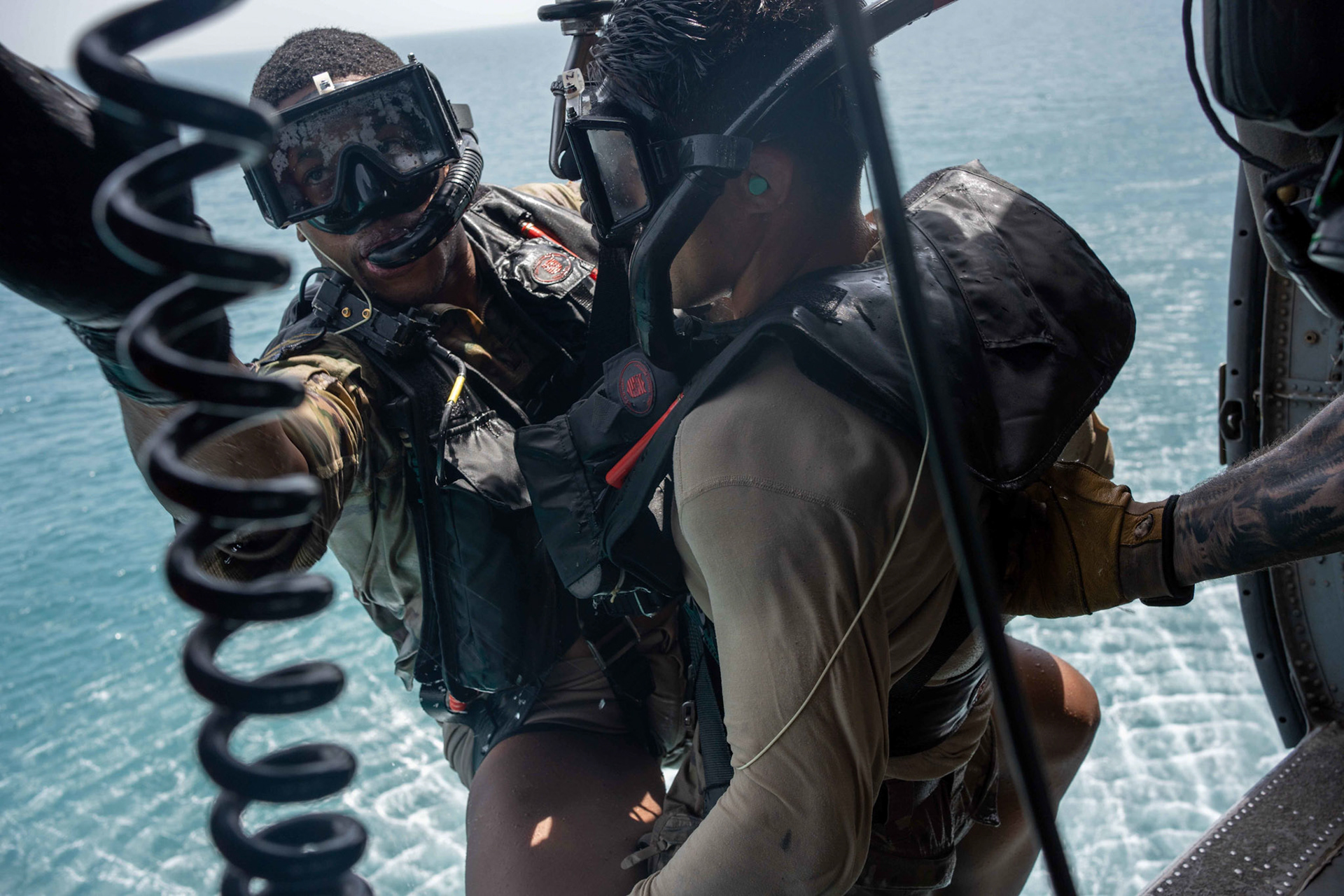 220511-A-YK067-1038 Naval Aircrewman (Helicopter) 2nd Class Hunter Hill, right, assigned to Helicopter Sea Combat Squadron (HSC) 26, pulls Naval Aircrewman (Helicopter) 3rd Class Elishua Hardy into an MH-60 Knighthawk during an at-sea search and rescue training operation during Exercise Neon Defender 2022. Neon Defender is an annual bilateral training event between U.S. Naval Forces Central Command and Bahrain. The exercise focuses on maritime security operations, installation defense and medical response. (U.S. Army photo by Sgt. Terry Vongsouthi)