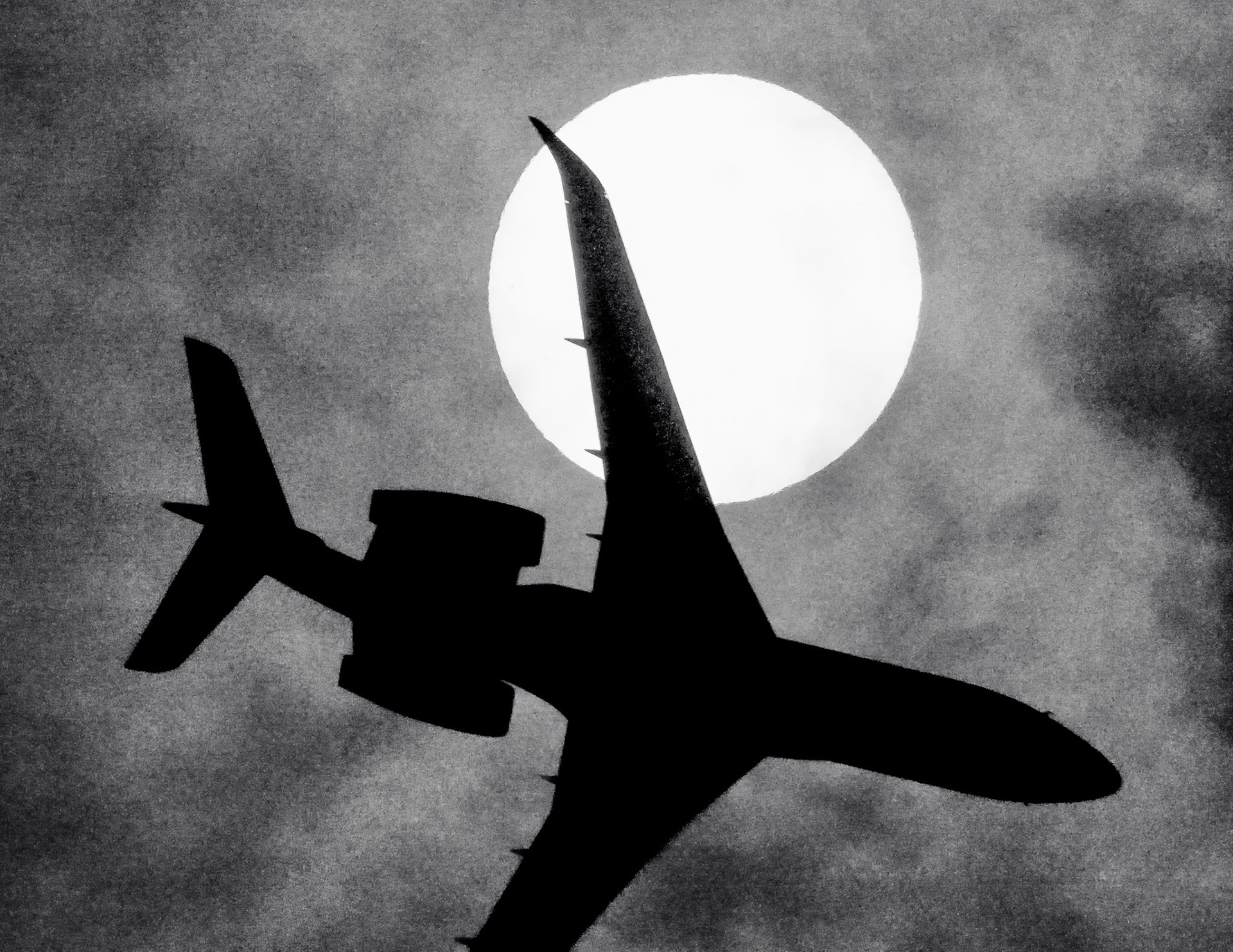 This was an entirely unintentional photo captured when I was watching a high-altitude flight, and the Sun went behind a fairly dense cloud. I pushed the ISO way up to 12800 to try and see the Sun through the nuisance clouds and the solar filter. I thought the plane I was tracking would be close to a solar transit, and while I had given up on a clear shot (insert "man shakes fist at cloud" image here), I still wanted to know if the Sun was above the flight path. Suddenly, from the east, I hear a jet, and in the blink of an eye, this shadowy plane zips across the viewfinder.According to Flightradar24.com, this is Embraer (Test) flight EMB163 traveling at 2,861 feet and 227 knots. It had left Melbourne Orlando International Airport - MLB 1:10 prior, and it was on approach to land at MLB after a test flight that included several racetrack-shaped loops over the Atlantic. Embraer builds and sells jets at their site here in Melbourne, so I assume this may have been a potential customer taking a multi-million dollar jet out for a test drive. I was shooting video; otherwise, I would never have caught the image. I was still at 1/4000 and f10, so the image is still pretty dark, and at ISO12800, the image is quite grainy, so it lent itself nicely to a moody black and white finish, presented here.