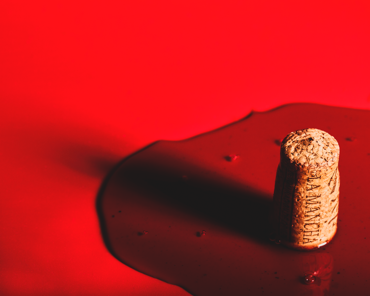 En esta ocasión el producto, el vino, se presenta de una forma diferente. La denominación de origen de La Mancha se puede leer en el corcho y el vino crea una "mancha" sobre fondo rojo intenso. Se ha dejado un espacio para texto en la parte superior izquierda ya que la idea es aplicar la imagen como ilustración para un cartel, un artículo, web...