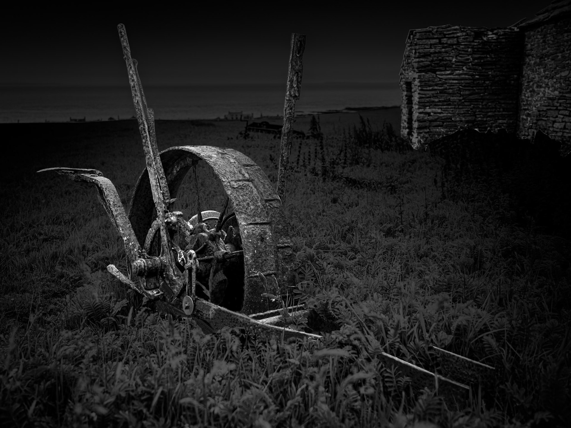 Agriculture has shaped Stroma's landscape for generations and, unlike the permanent settlement, farming has not entirely disappeared from the island. Scattered among the crofts are older pieces of agricultural machinery whose working lives have ended, gradually deteriorating where they were left. I am fascinated by these objects because they provide a direct physical connection with labour. The twisted metal, wheels and mechanisms speak of people working this land rather than simply inhabiting it. In this photograph I have used light selectively to draw the machinery from the surrounding vegetation while retaining the darkness of the wider landscape. It becomes almost sculptural, but its decay remains visible: another layer in Stroma's accumulation of human traces, existing alongside the continuing agricultural use of the island.Stroma is an ongoing photographic project which I am currently developing.
