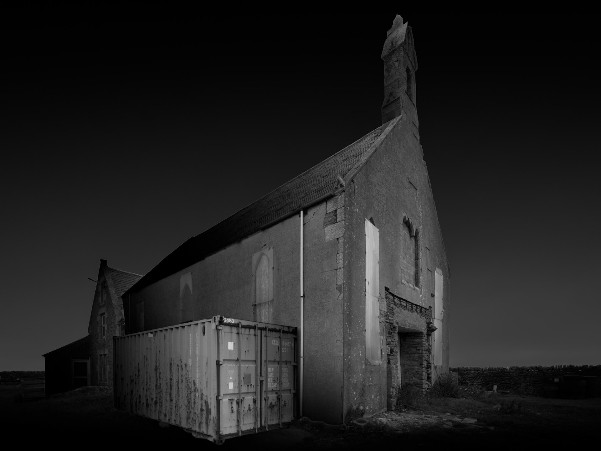The church was once at the heart of Stroma's community, serving a population scattered among the island's crofts. Its scale and distinctive architecture give some indication of a settlement that was considerably more substantial than the handful of surviving intact buildings might now suggest. As Stroma's population declined, the institutions that supported communal life inevitably declined with it, and the church eventually closed. I wanted to photograph the building with a monumentality that reflects its former significance rather than treating it simply as another abandoned structure. Its gable and long walls rise dramatically against the dark sky, while the modern container alongside it introduces a deliberately awkward reminder that contemporary agricultural activity continues around these remnants of the former community.Stroma is an ongoing photographic project which I am currently developing.
