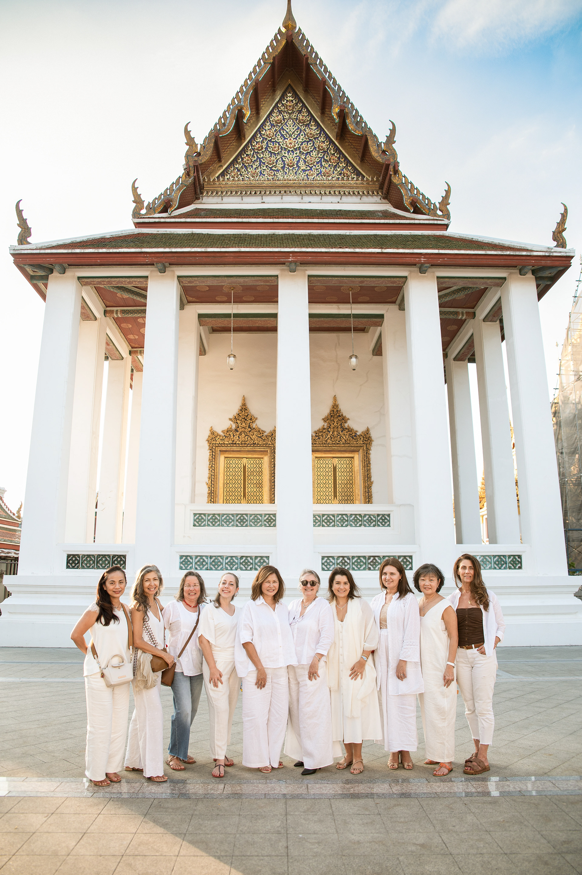 A large group of women in white outfits posing in front of a traditional Thai temple in Bangkok, professional group portrait photography by a local Bangkok photographer.