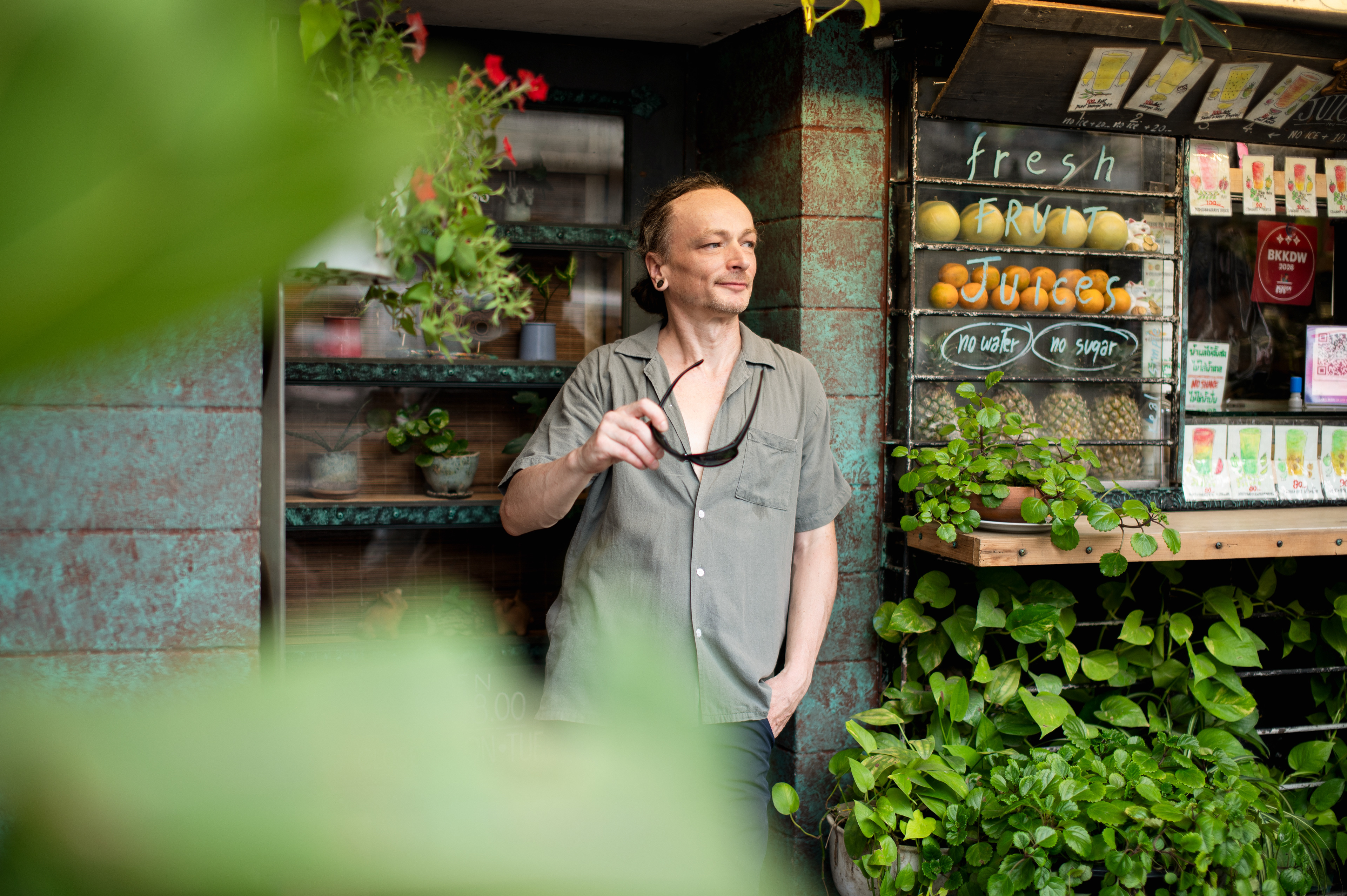 Man posing by a fresh fruit juice stall in a Bangkok street, professional environmental portrait photography by a local lifestyle photographer.