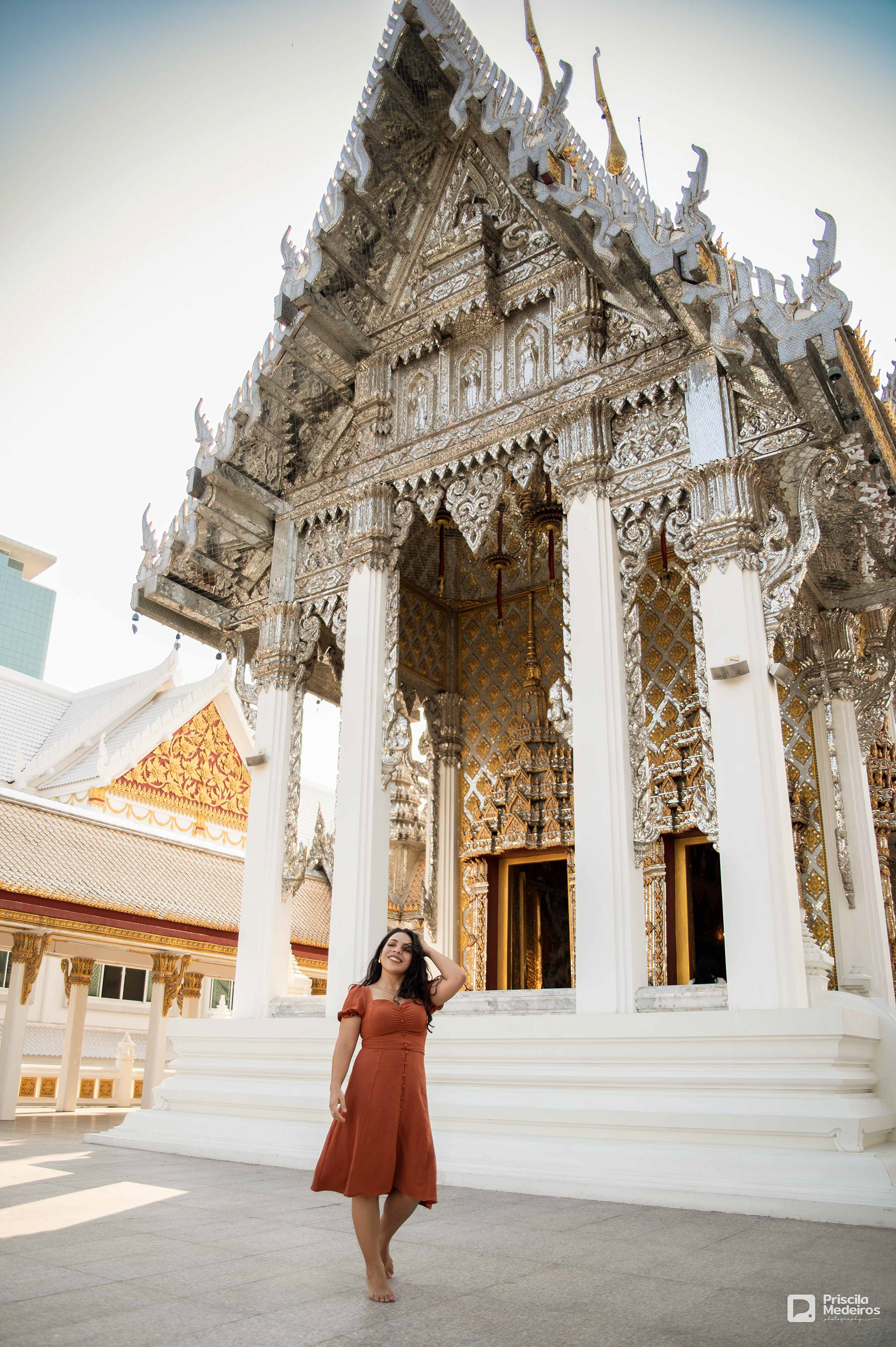 A woman smiling at a beautiful, intricate Thai temple in Bangkok, captured by a professional photographer.