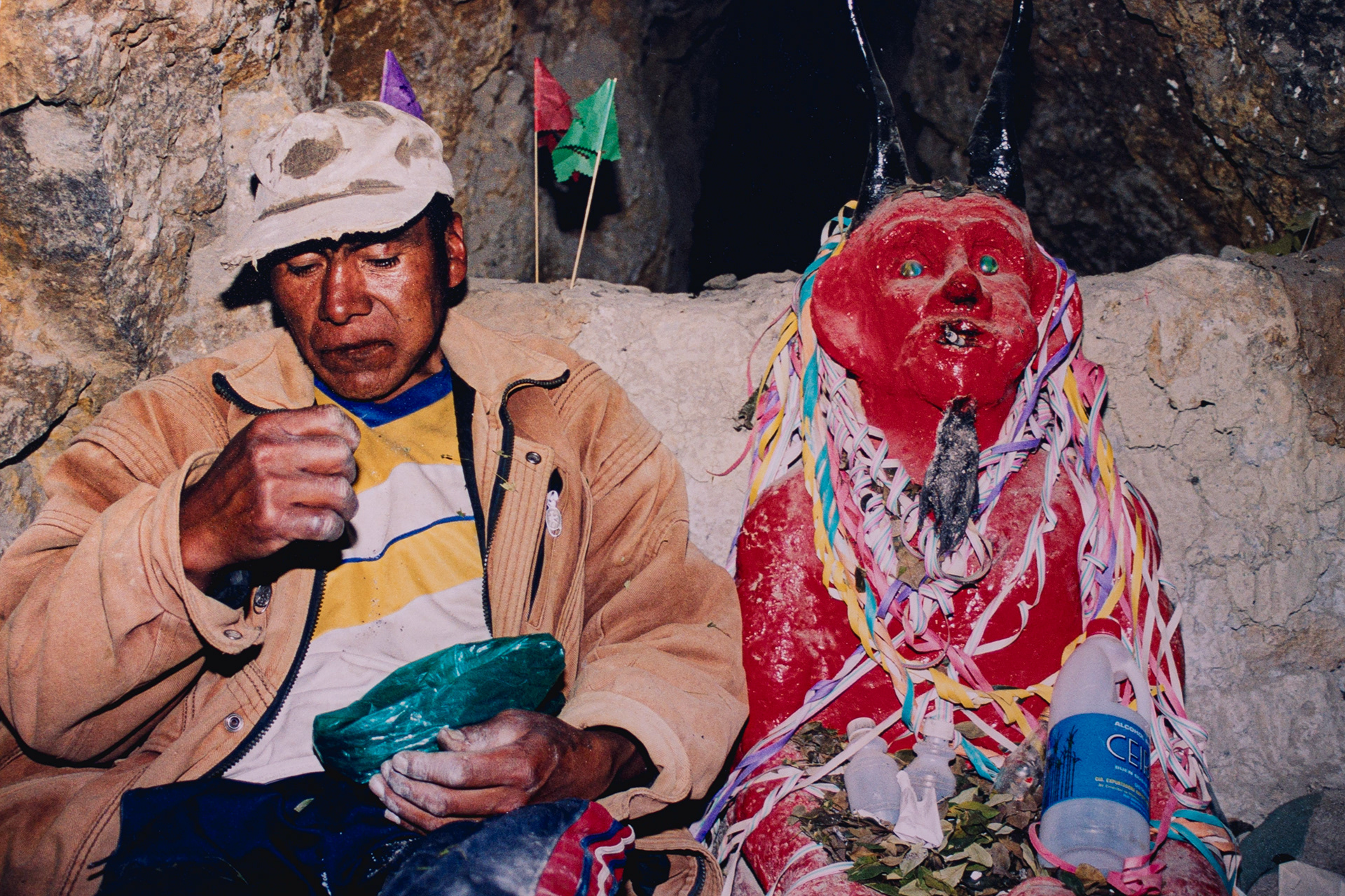 Un minero masca coca junto a El Tío, protector de la mina y de los trabajadores. Es normal que le lleven alcohol puro, cigarrillos y también dinamita y hojas de coca, con la esperanza de tener protección contra accidentes y que los ayude a encontrar una veta oculta que les de algo de riqueza.