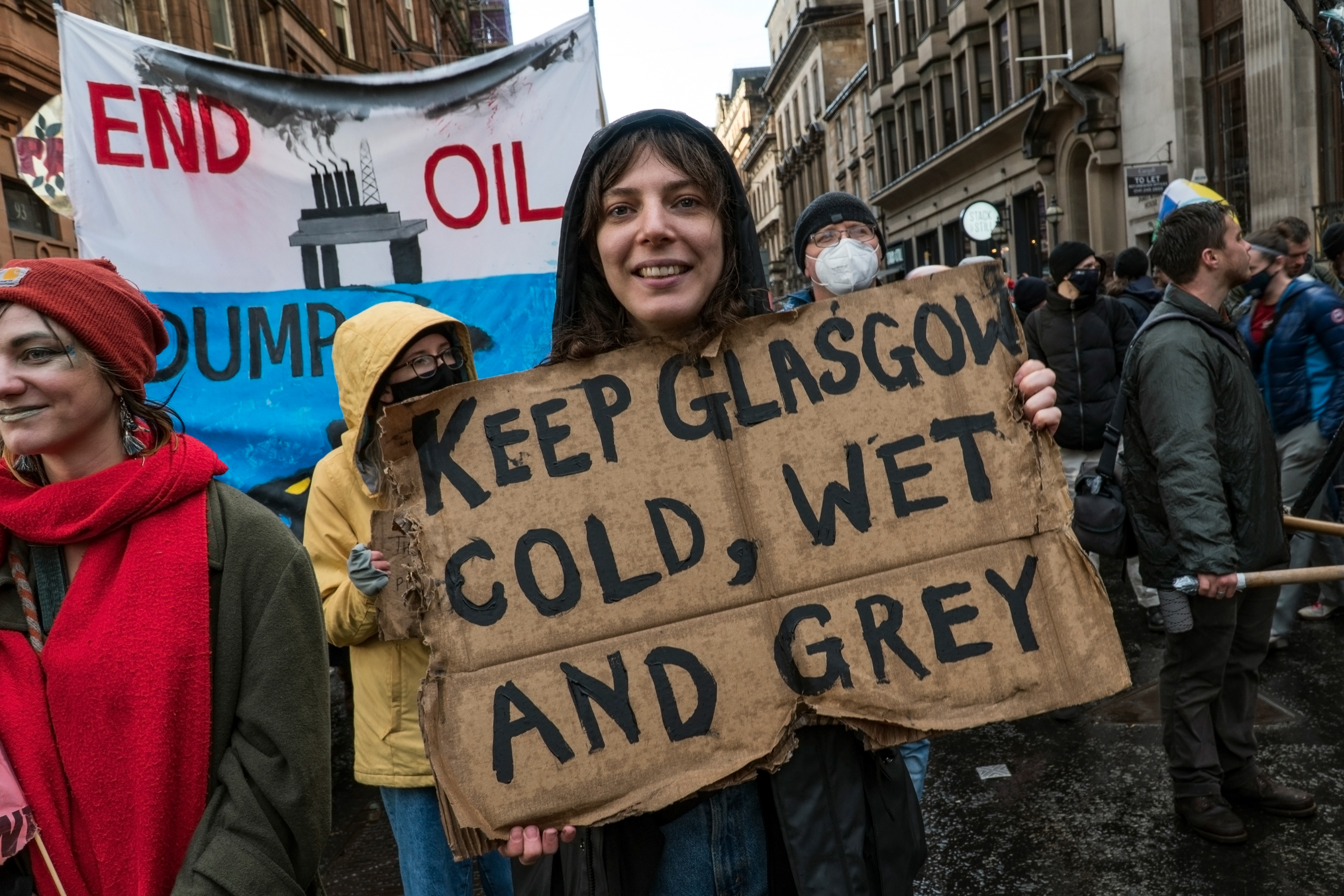 Image of demonstrator in Glasgow city centre during COP26, holding a slightly soggy sign 'Keep Glasgow cold, wet and grey'