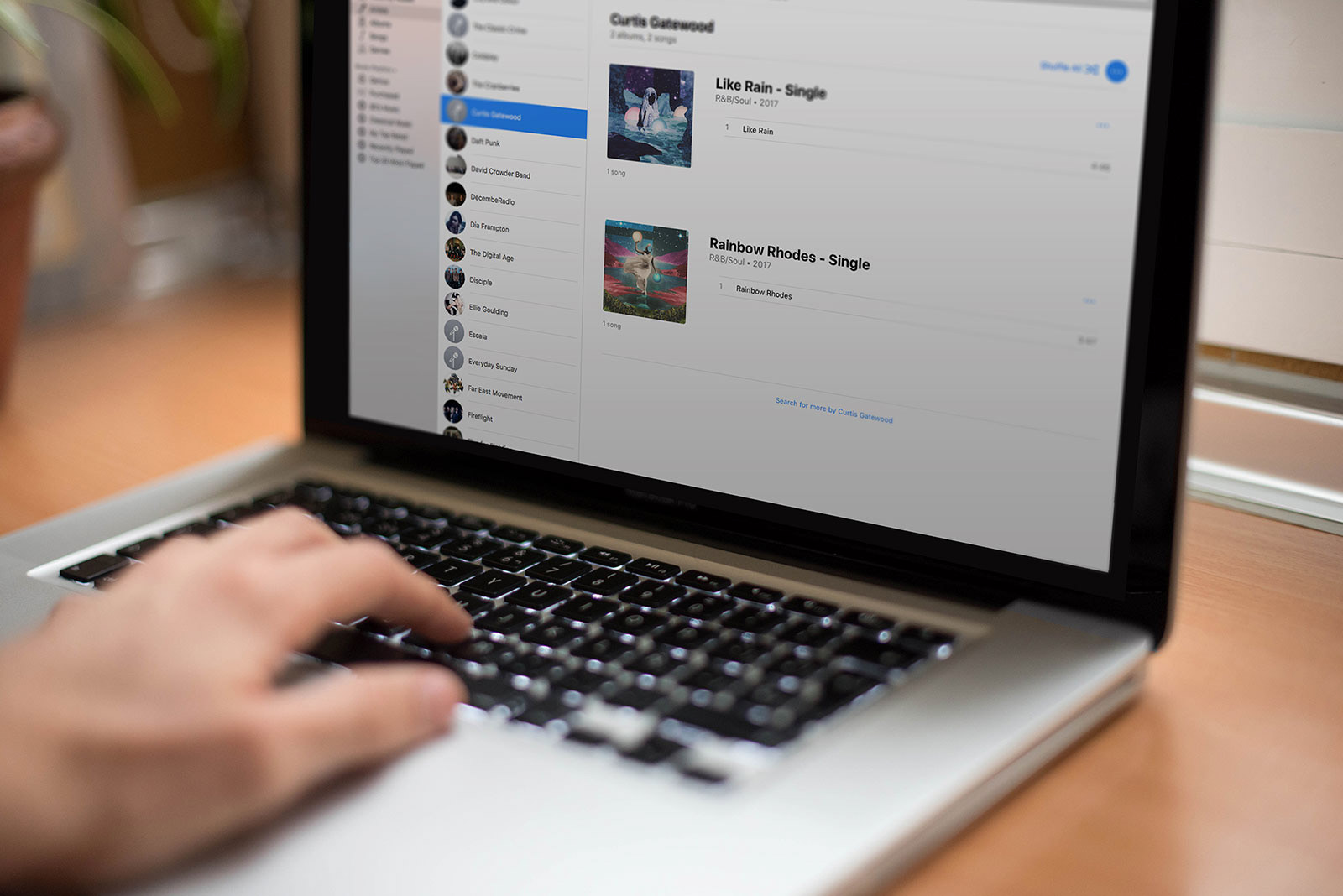 Laptop running the computer application iTunes. On the screen there is an image of Curtis Gatewood's "Like Rain" and "Rainbow Rhodes" album artwork.