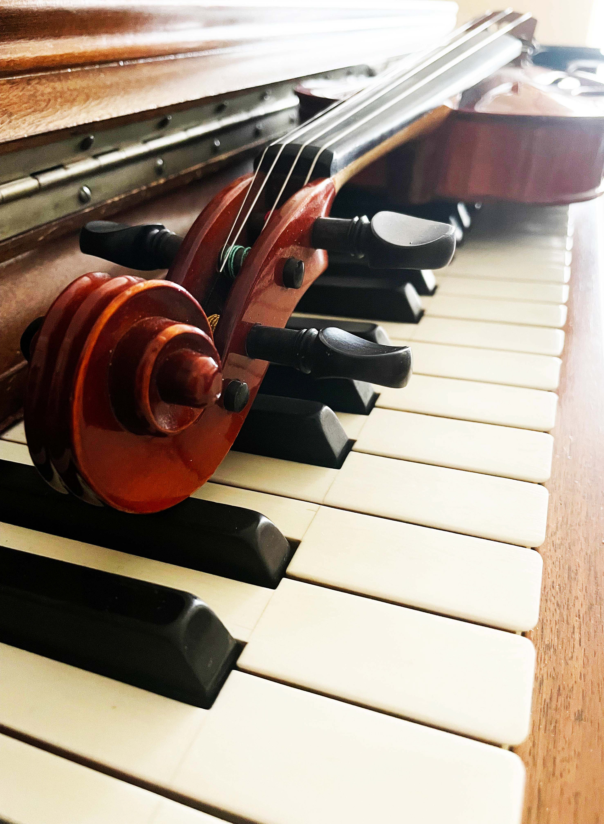 Violin with scroll facing towards camera, lying on piano keys, shown at an angle and close up.