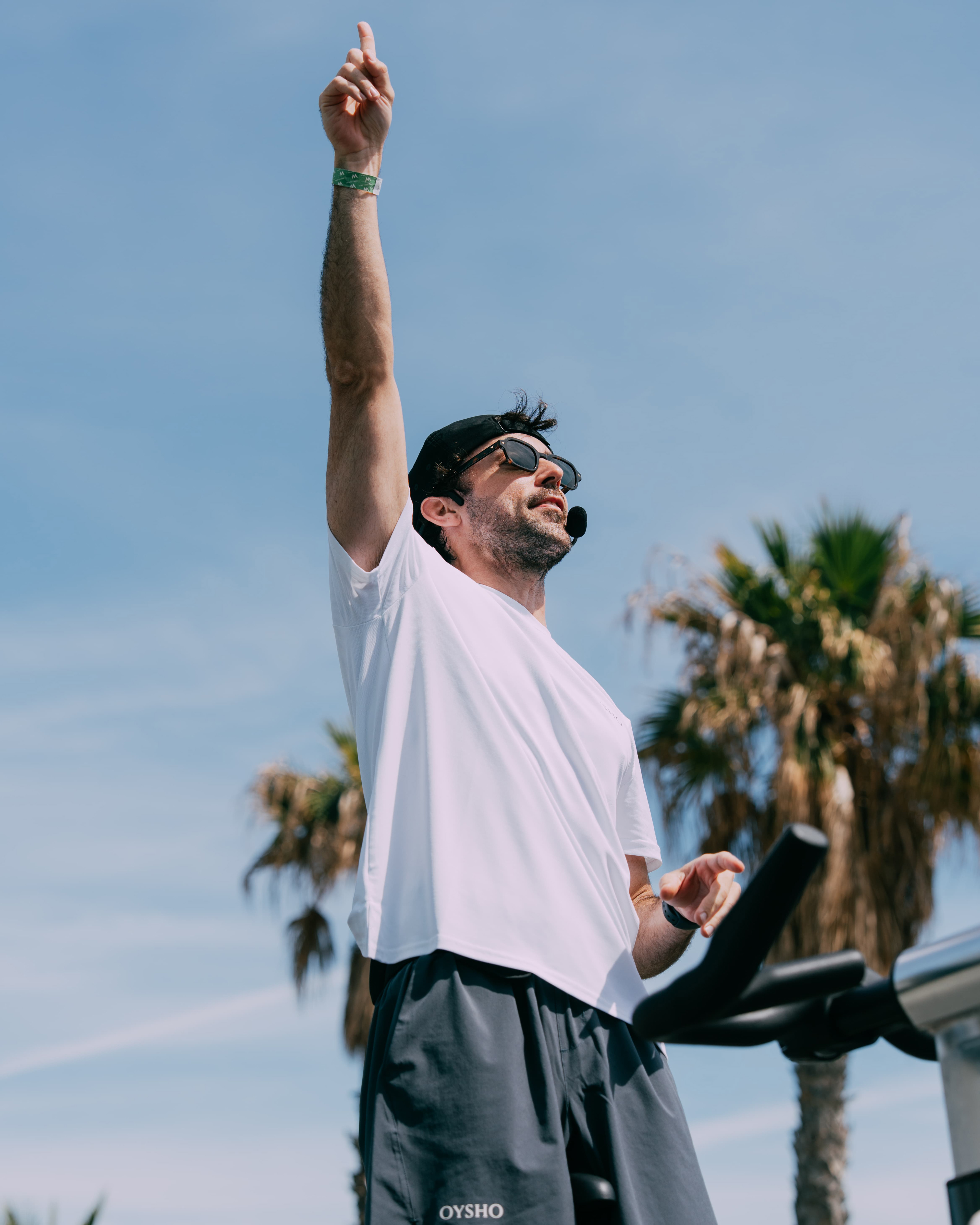 Cycling instructor with arm raised under palm trees, Oysho x Lovecycle