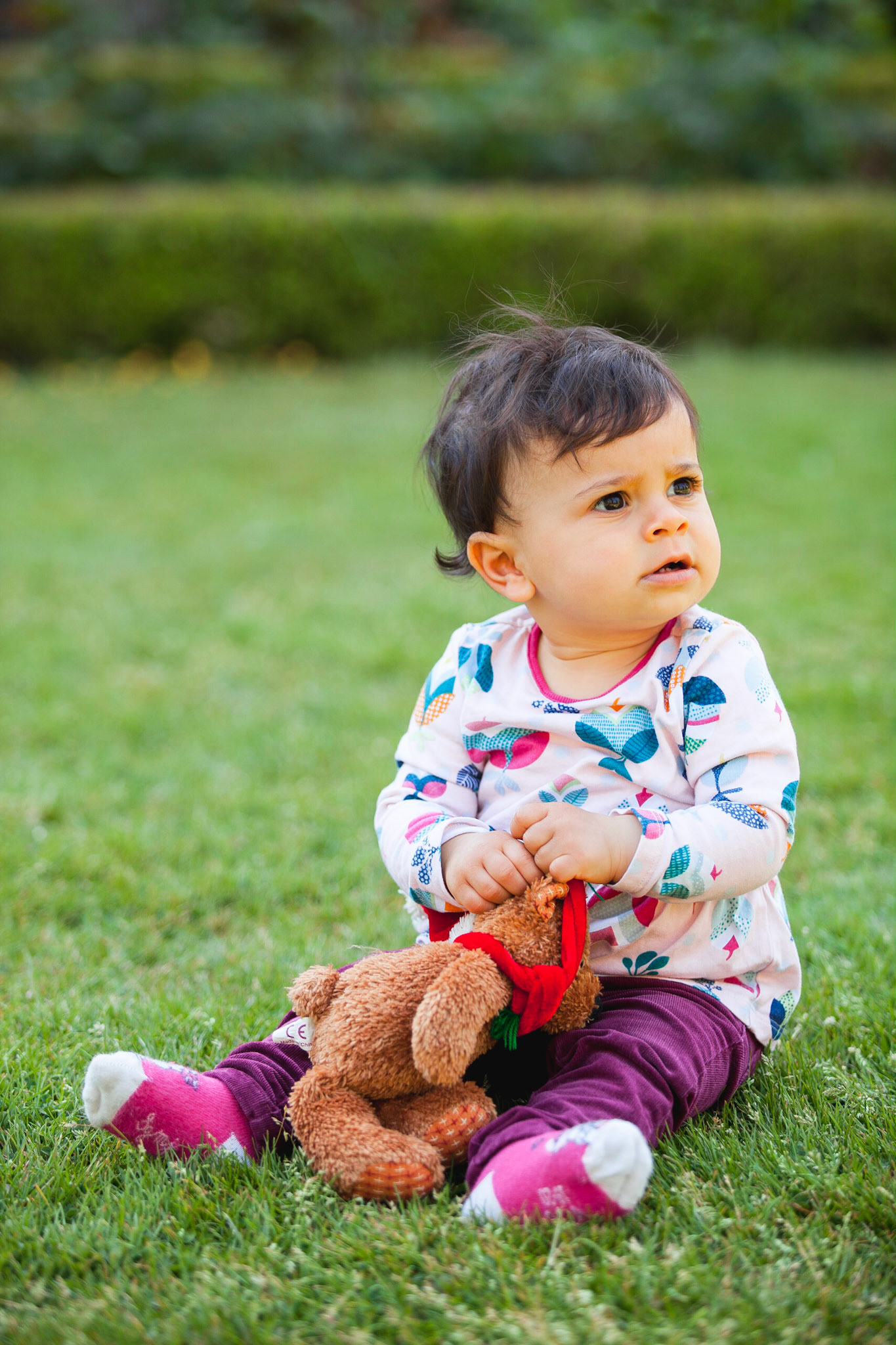 Petite fille assise dans un parc avec un nounours dans les mains. Photo couleur.