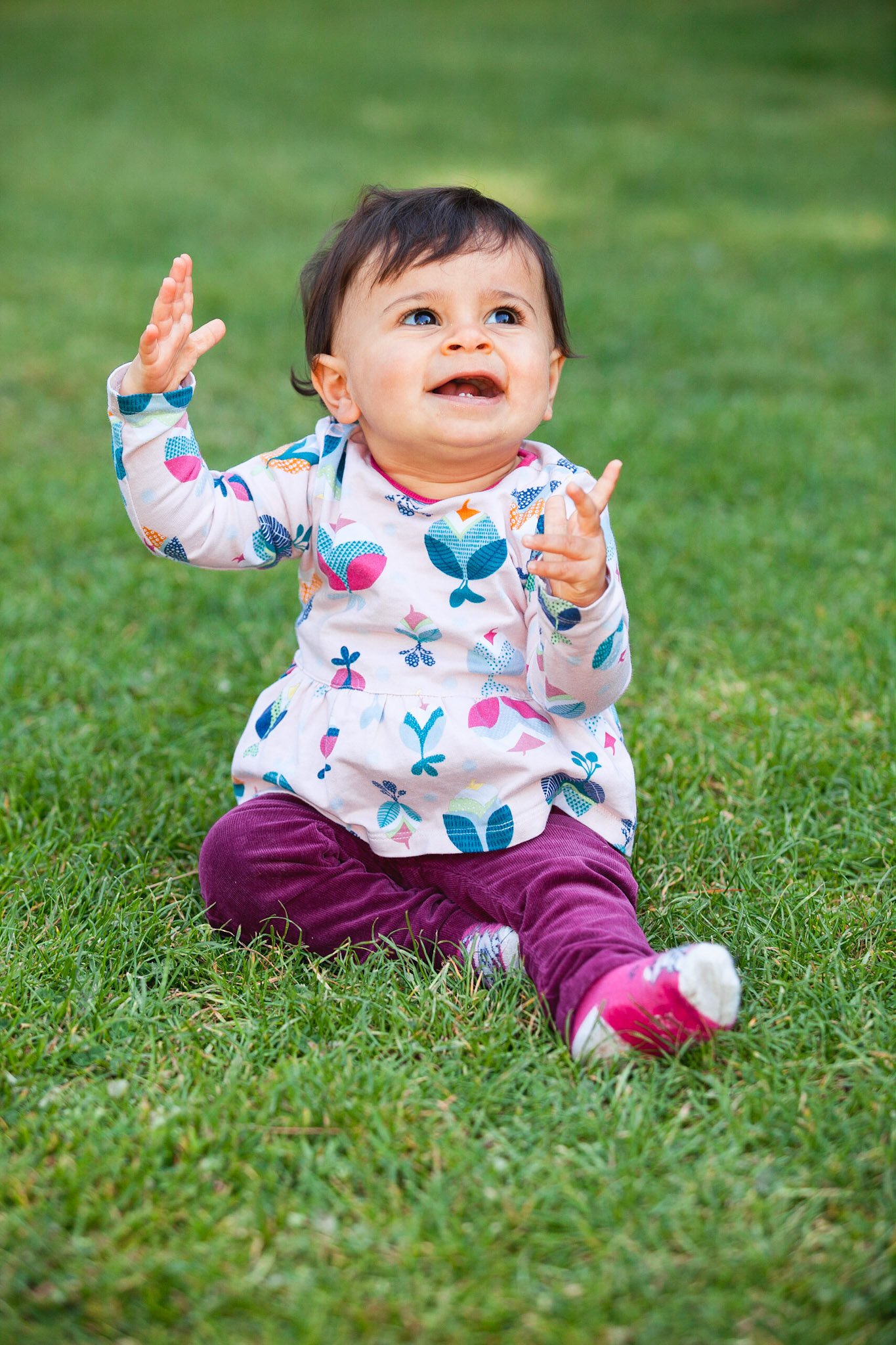 Petite fille qui sourit, assise par terre dans un parc. Photo couleur.