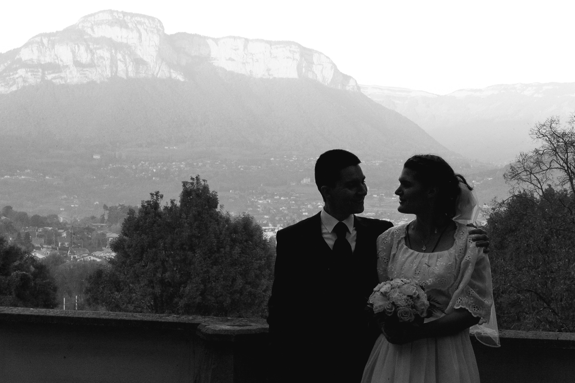 Silhouette de jeunes mariés enlacés devant une montagne. Photo noir et blanc.