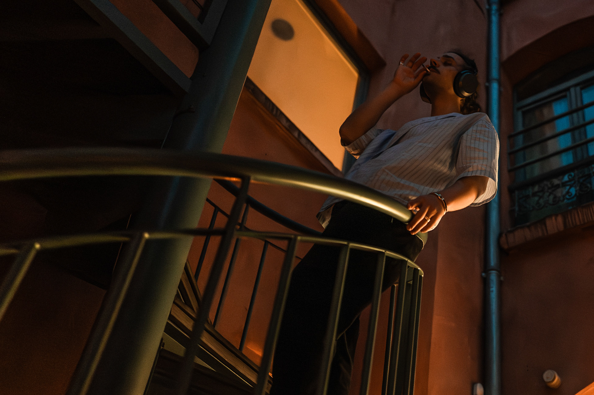 Nimrod stands on the AEPP terrace at night, wearing headphones and lost in his thoughts. He takes a quiet moment to himself, smoking as he looks out into the distance. The scene captures a sense of solitude and introspection, as he disconnects from his surroundings and drifts into his own world. Picture taken the 2026-04-14©Aurora Ghigino