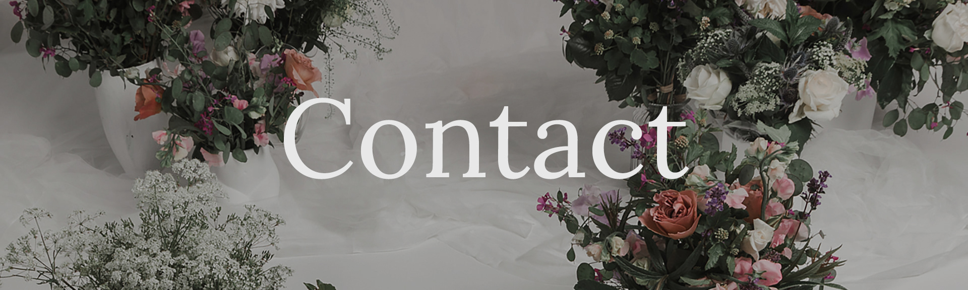 A header image for the Contact page. It shows a floral arrangement on soft white fabric.