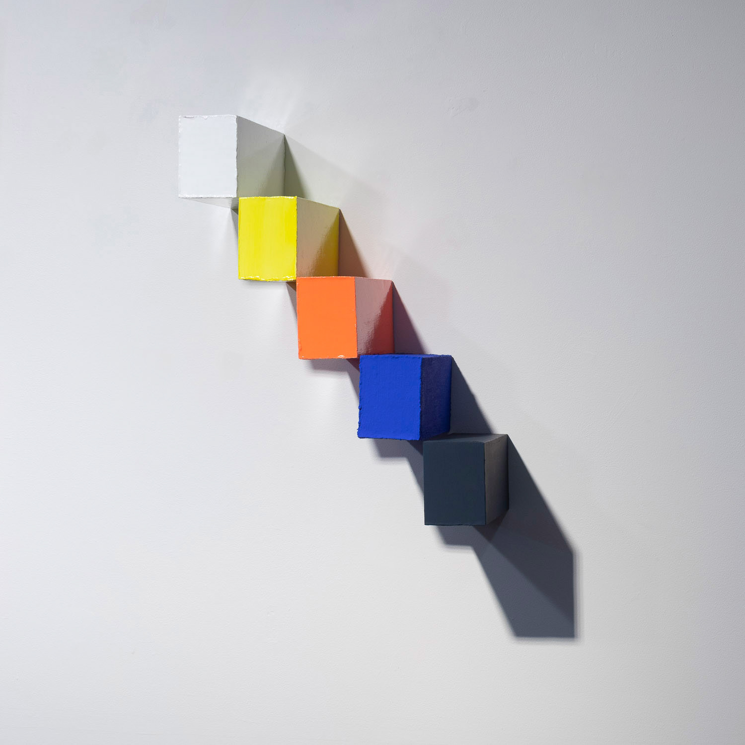 five brick shaped colourful blocks hung on a white wall in a staircase formation