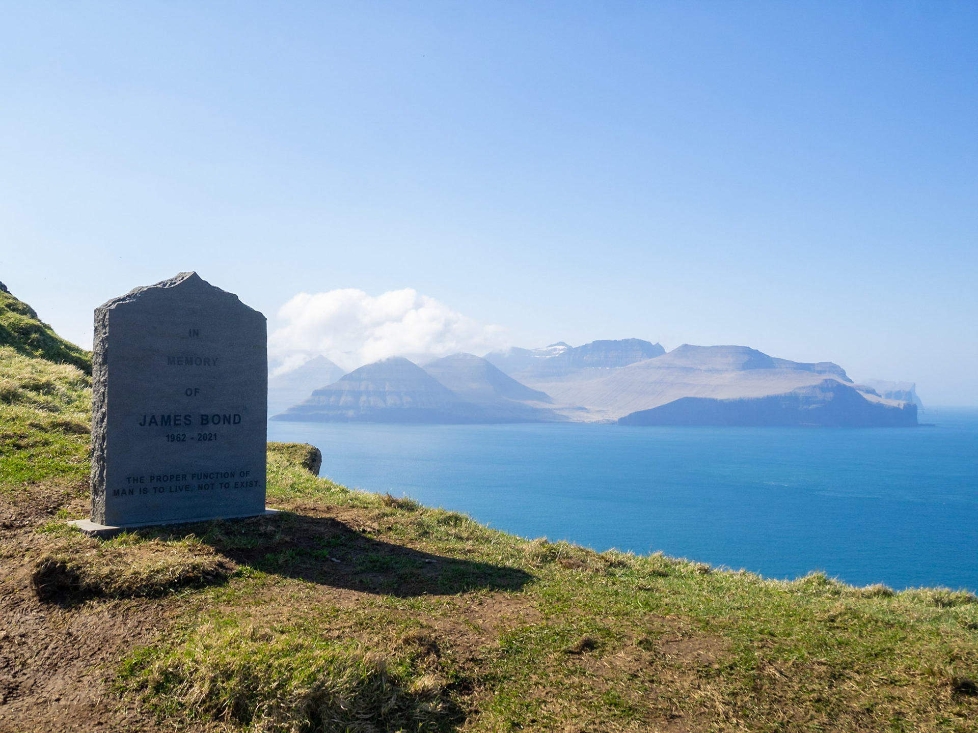 James Bon grave stone by the cliffs edge in Kalsoy island with Eysturoy in background