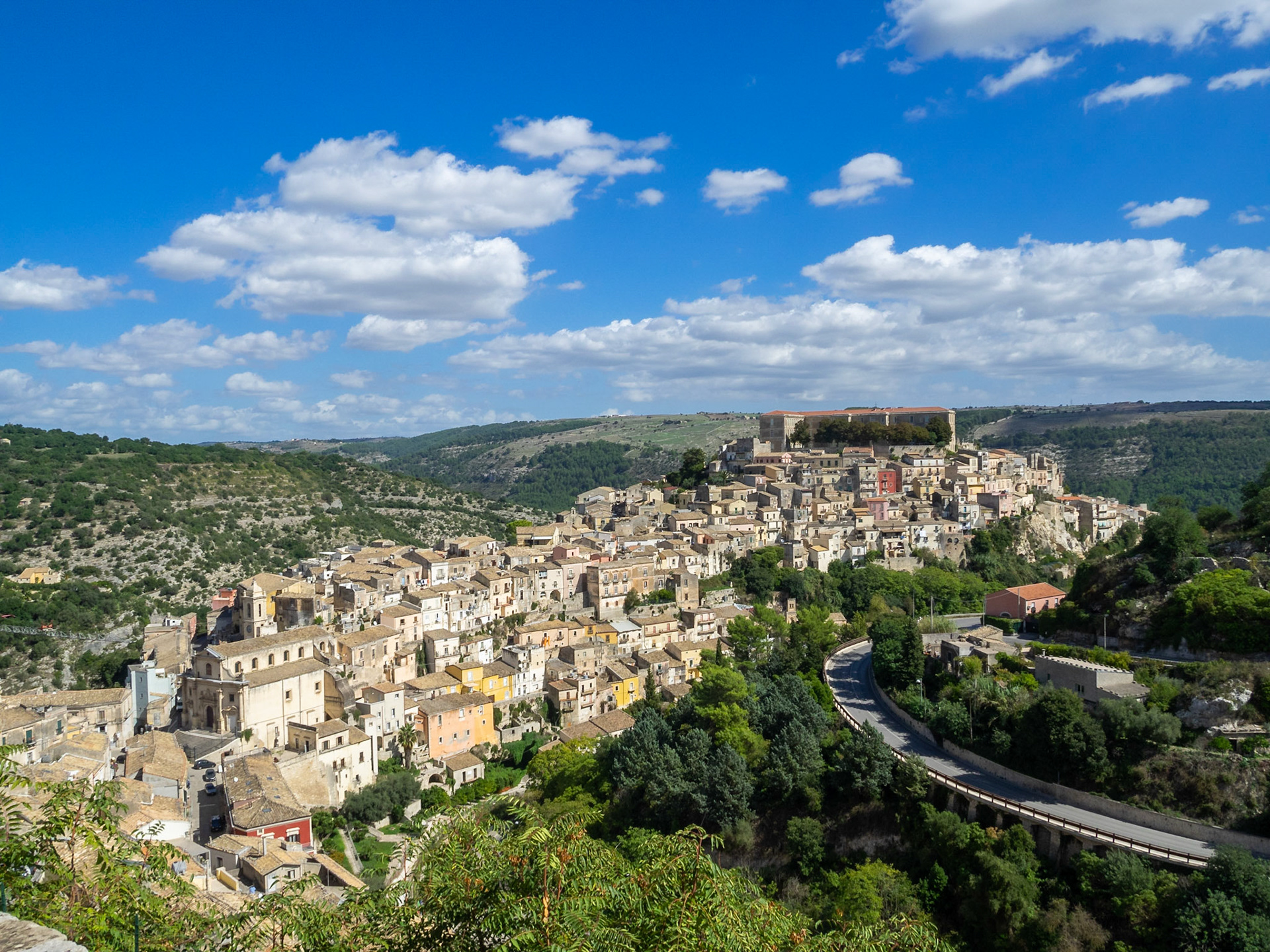 Ragusa Ibla between the green mountains and the blue sky over Valle dei Ponti