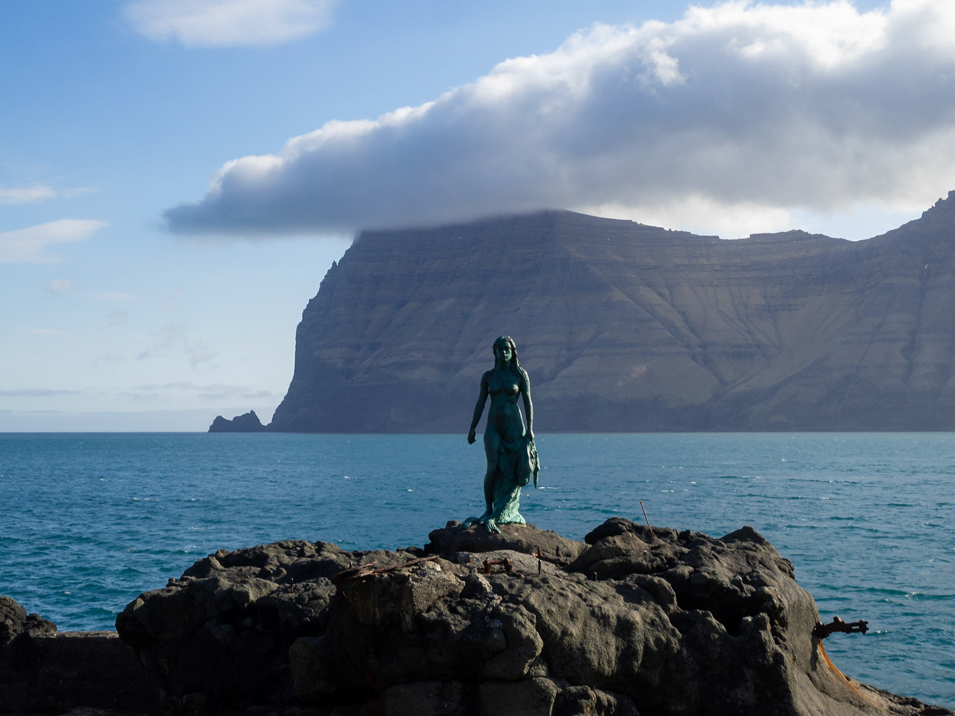 Kópakonan, the seal woman, statue over the rocks by the Kalsoyarfjørður fjord with Kynoy island in background
