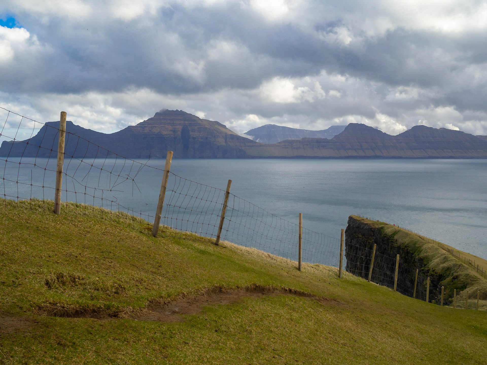 Hiking path by the cliffs up to Fjallið maountain with Kalsoy island in background