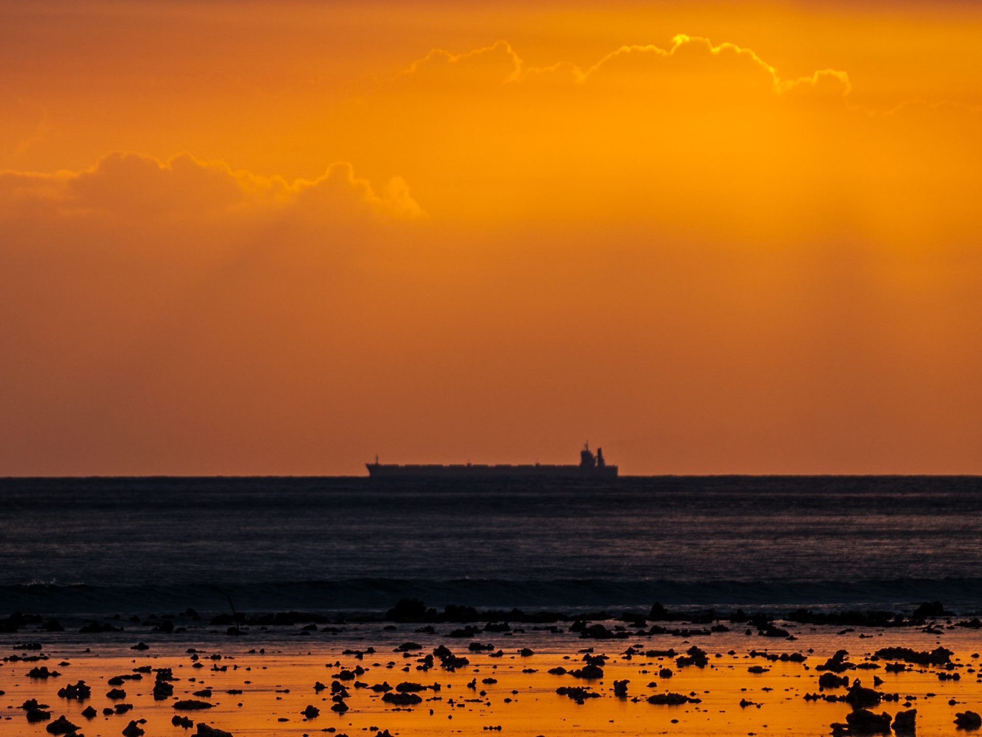Cargo ship silhouette in the horizon line with sunset orange light