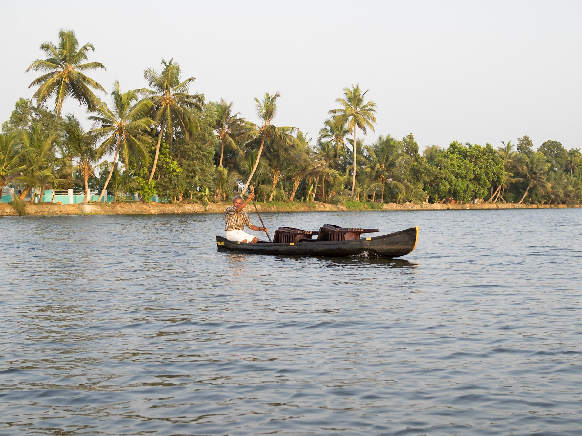 A man crosses in his canoe a wide canal in Kerala backwaters